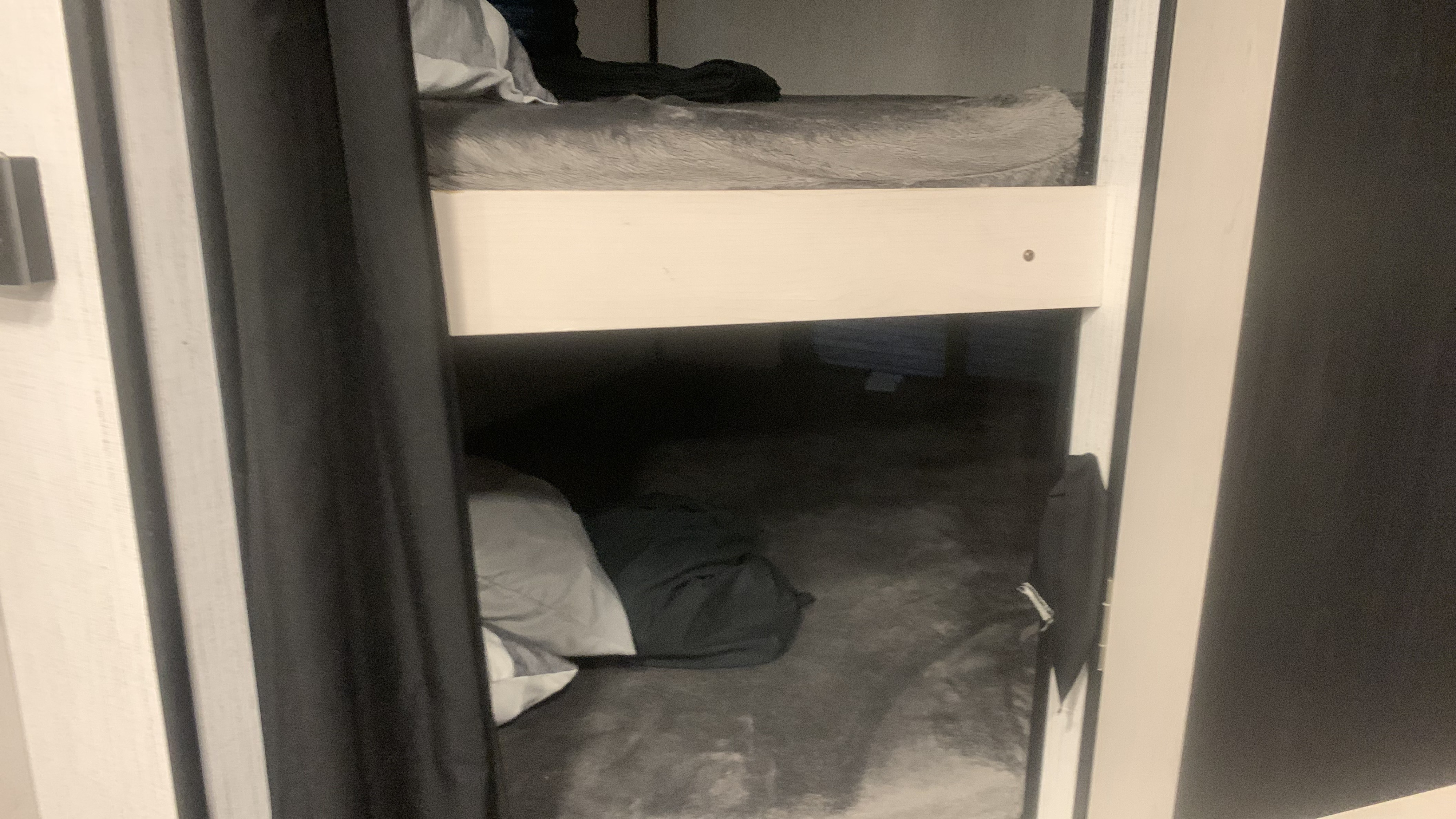 Interior of an RV rental showing stacked bunk beds with privacy curtains. The top bunk has a grey mattress, while the lower is a dark sleeping area.. Heartland m 2022