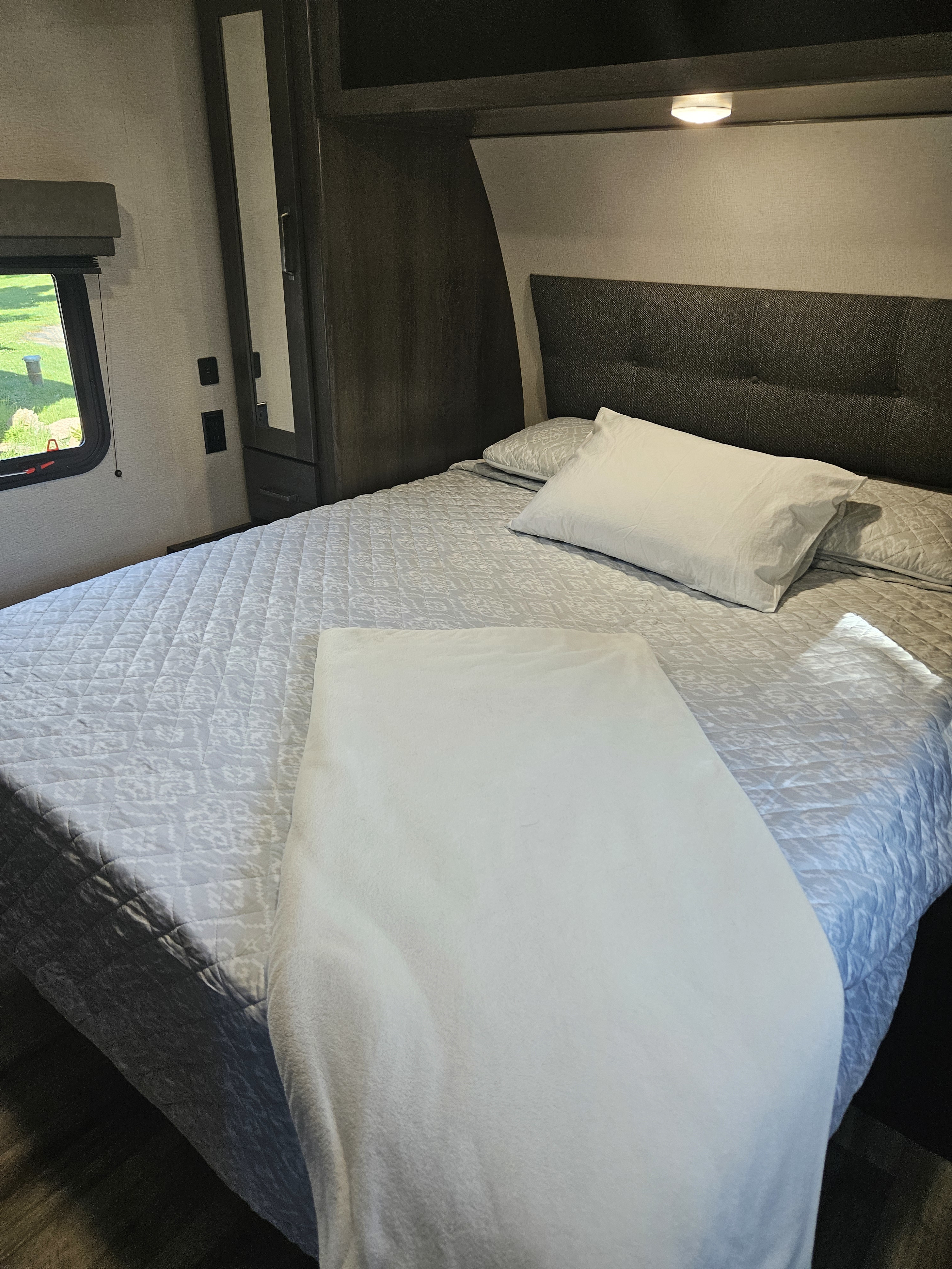 Inside a cozy RV rental bedroom: A comfortable bed with soft bedding, built-in storage, and window view.. Grand Design Transcend Xplor 2023
