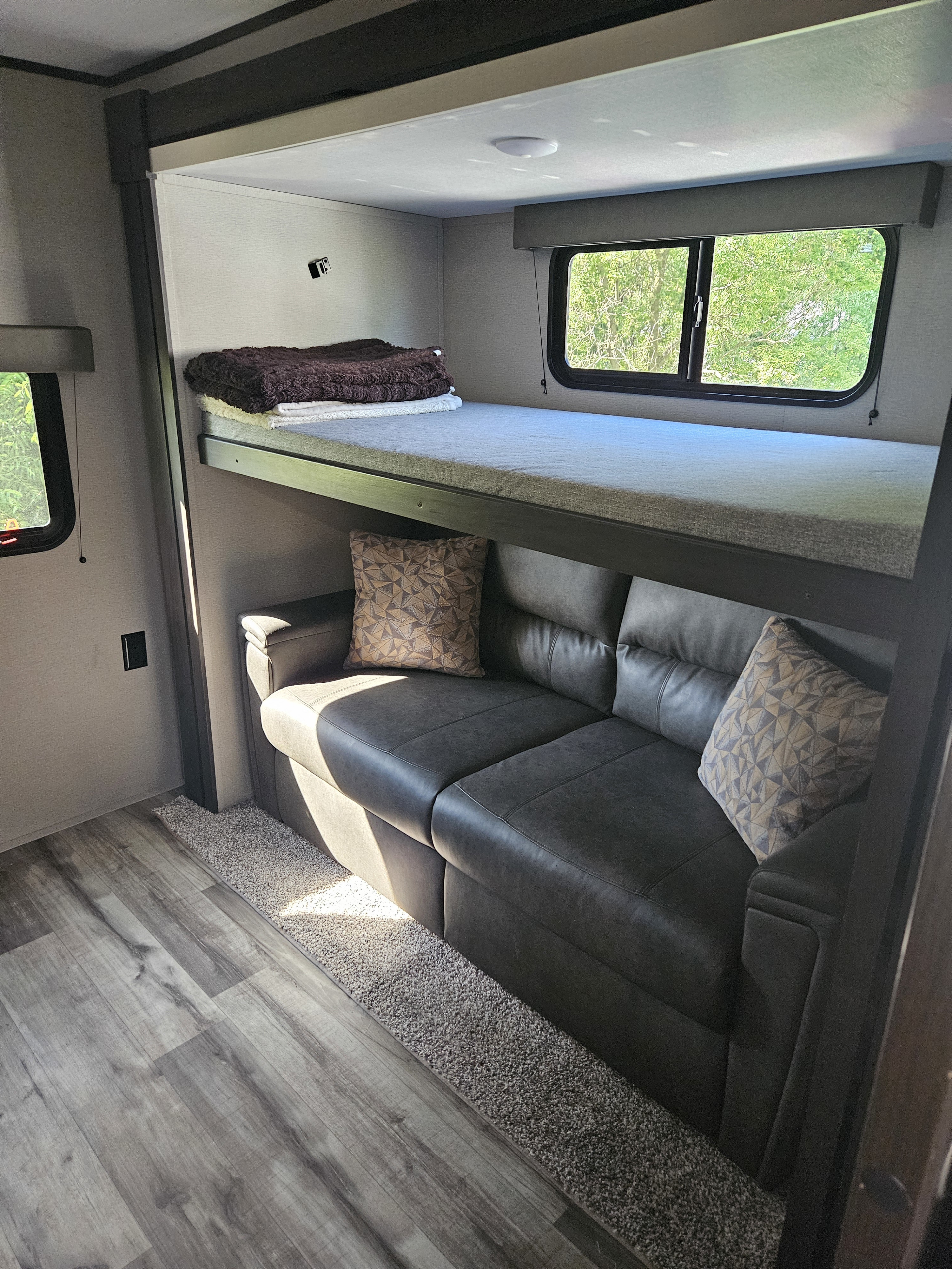 RV rental interior: A bunk bed is positioned above a dark sofa, with wood-look flooring. Ideal for compact travel.. Grand Design Transcend Xplor 2023