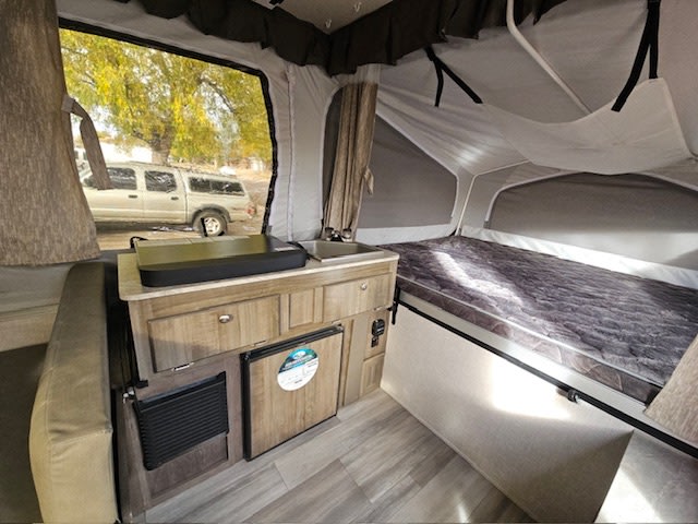 Pop-up RV rental interior: compact kitchen, bed, and scenic window. Cozy setup for your camping adventures.. Forest River Rockwood ESP 2022