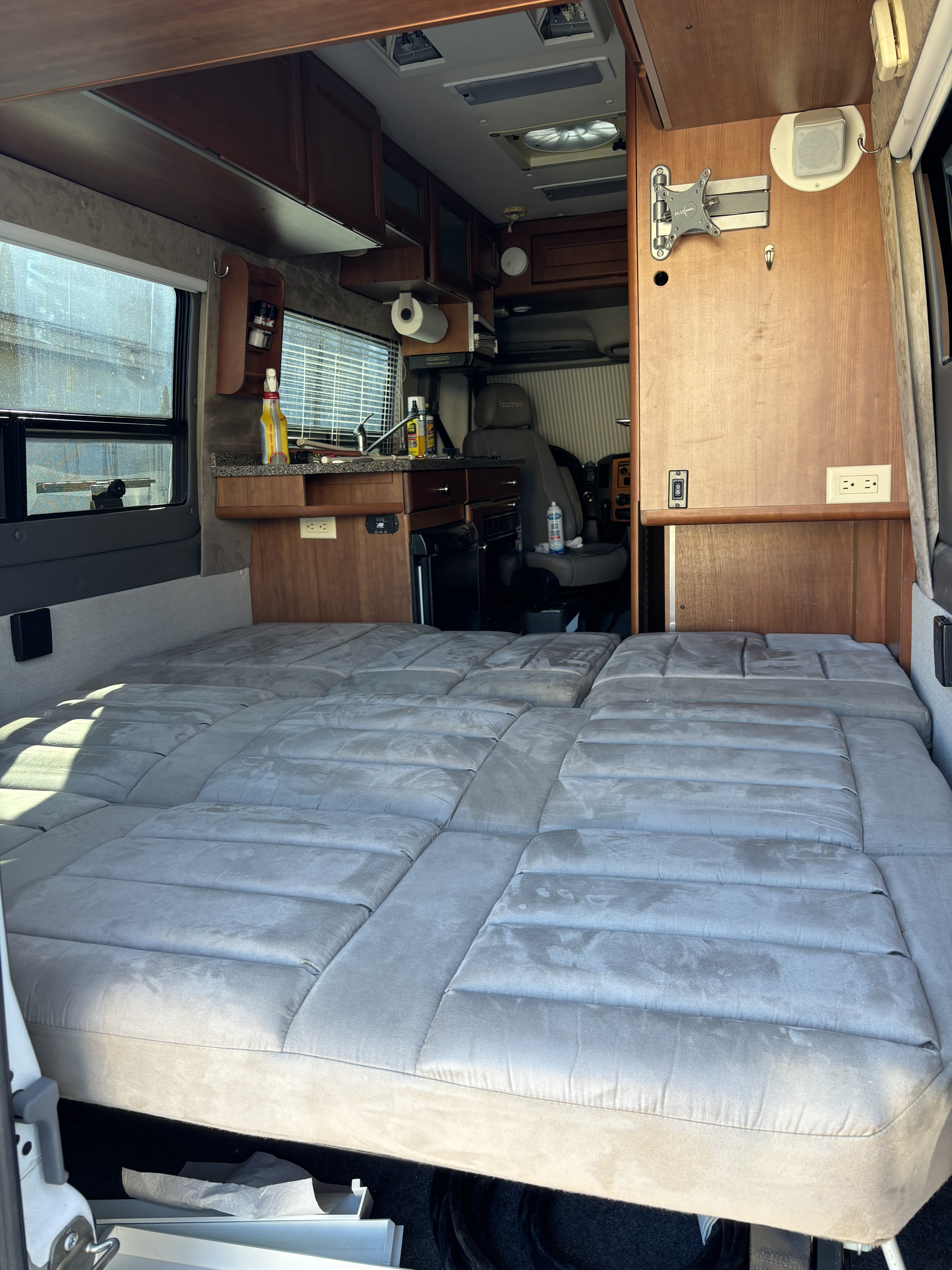 RV rental interior: A large grey convertible bed fills the space, with a compact kitchen and driver's area visible beyond.. Roadtrek Roadtrek Class B 2008