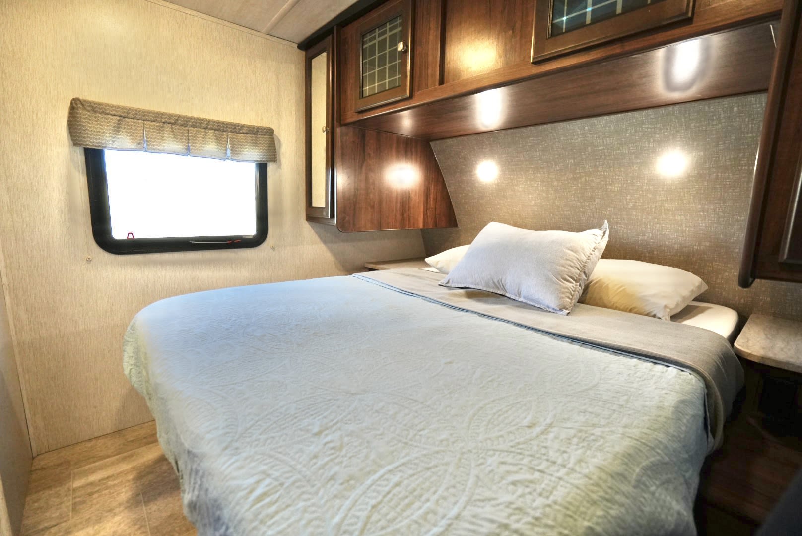 This cozy RV rental bedroom features a queen bed with built-in storage, a window, and reading lights, set in a compact space.. Heartland RVs Mallard 2019
