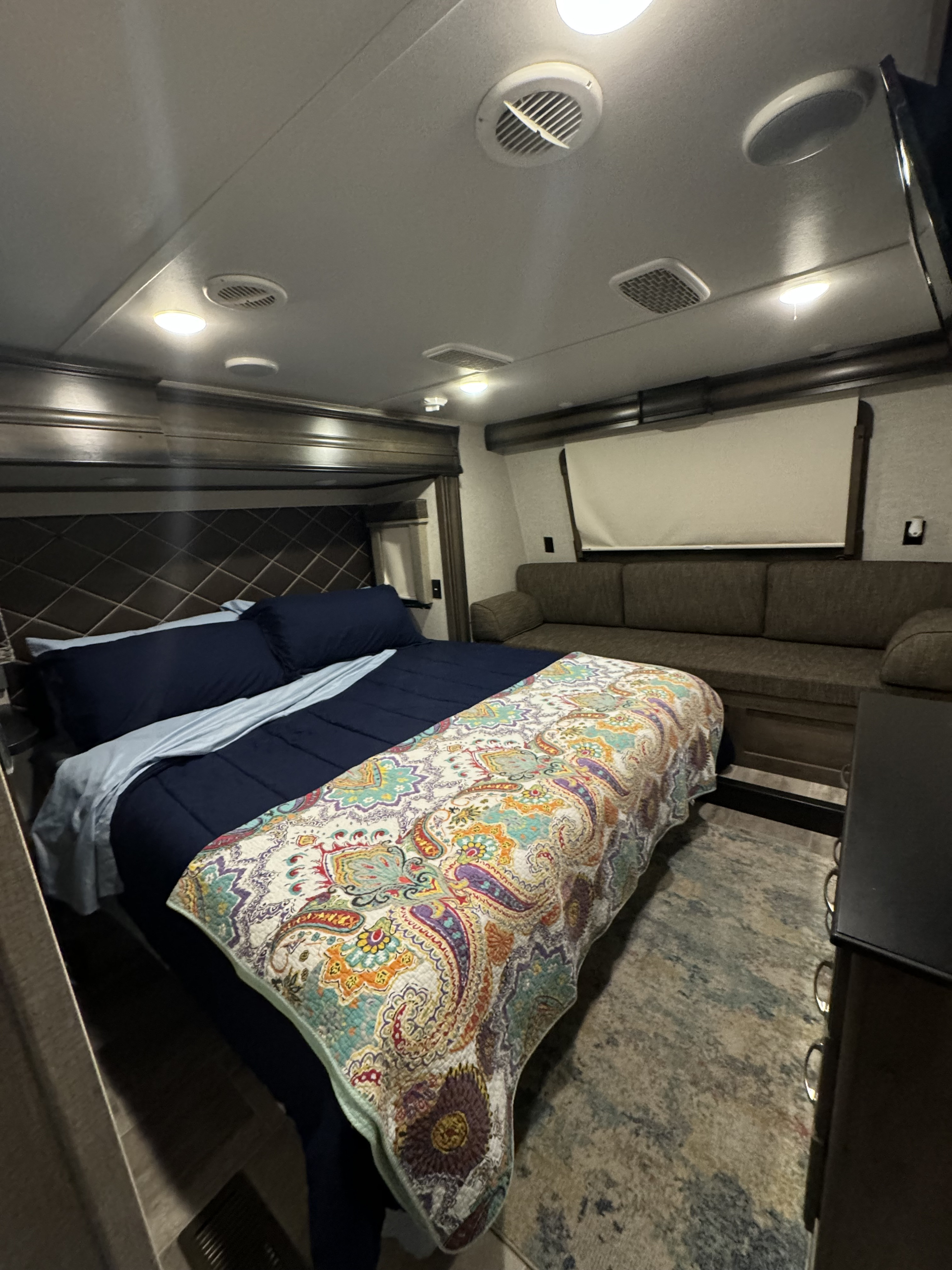 Spacious RV rental interior: bedroom with navy bedding, vibrant quilt, and cozy living room sofa for comfortable stays.. Keystone RV Montana 20th Anniversary 2019