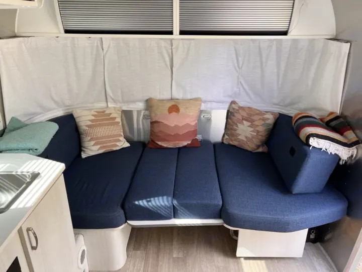 RV rental interior: Cozy blue sofa with colorful throw pillows & blankets in a camper dinette, ready for relaxation.. Airstream Airstream 2020