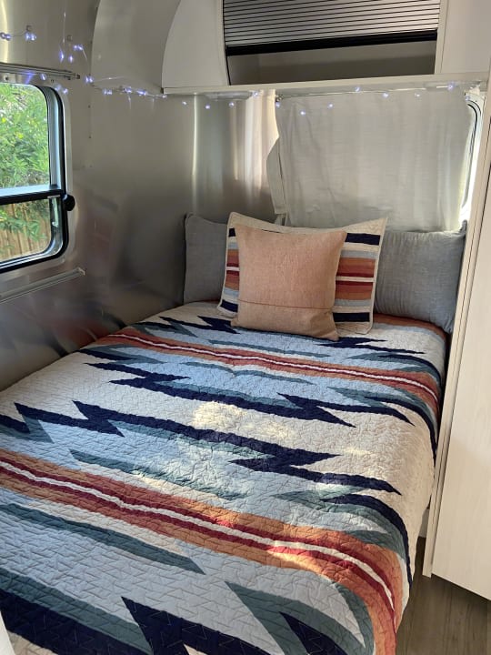 Inside a comfortable rv rental: a bed with a vibrant Southwestern quilt, soft pillows, and twinkling fairy lights.. Airstream Airstream 2020