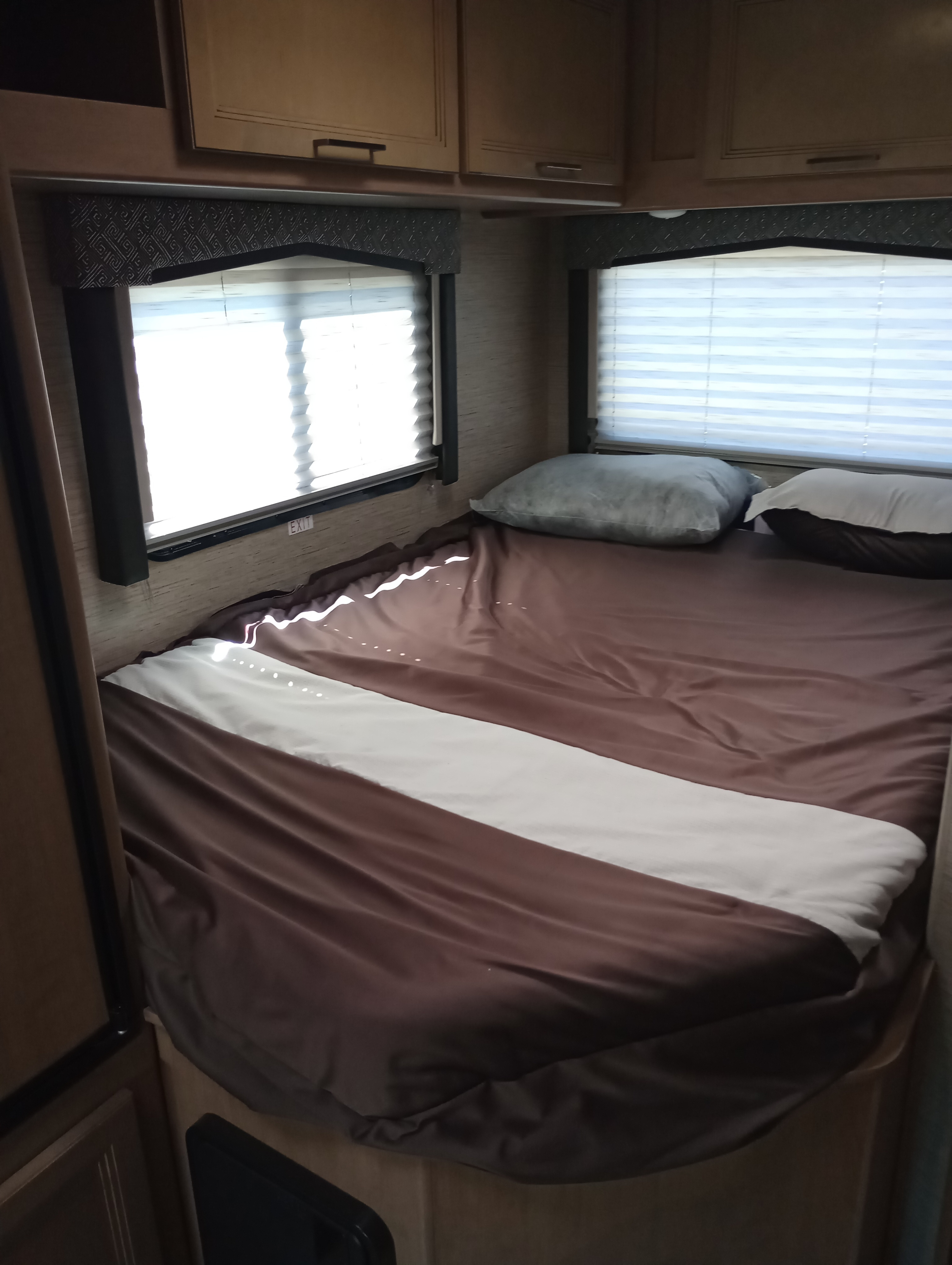Cozy RV rental bedroom with a made bed, brown & white bedding, window blinds, and overhead cabinets.. Thor Chateau 2022