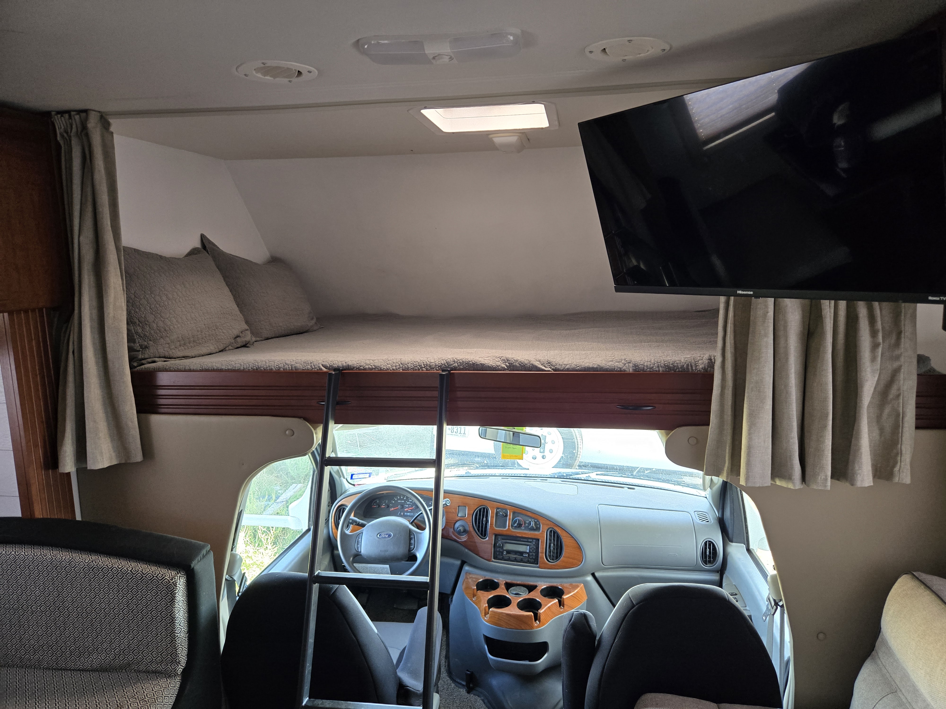 View inside an RV rental showing an overhead cab-over bed with ladder, a wall-mounted TV, and the driver's cockpit.. Thor Motor Coach Chateau 2007