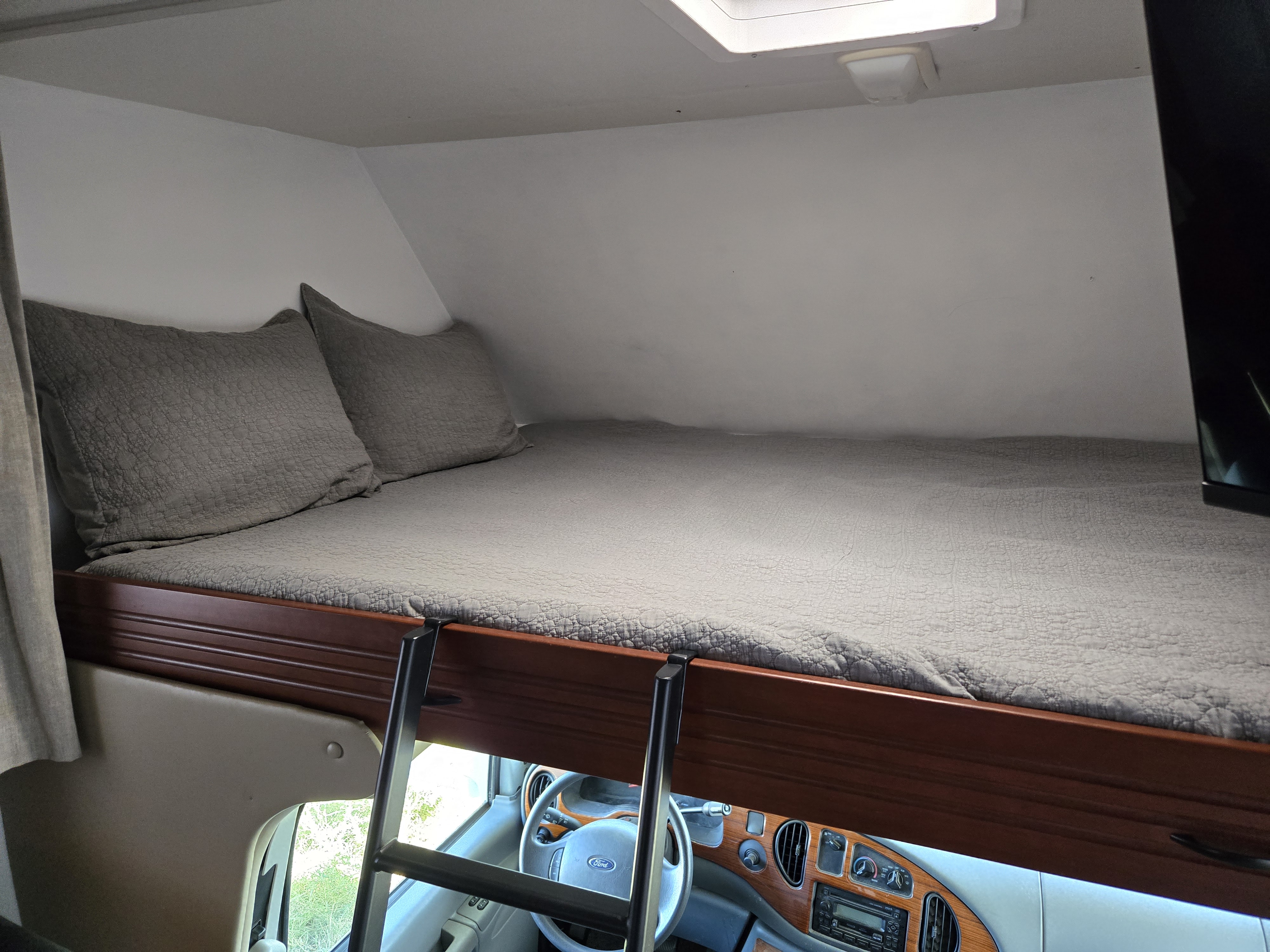 Cozy RV rental overhead bunk bed with ladder, pillows, and a view of the Ford dashboard from below.. Thor Motor Coach Chateau 2007