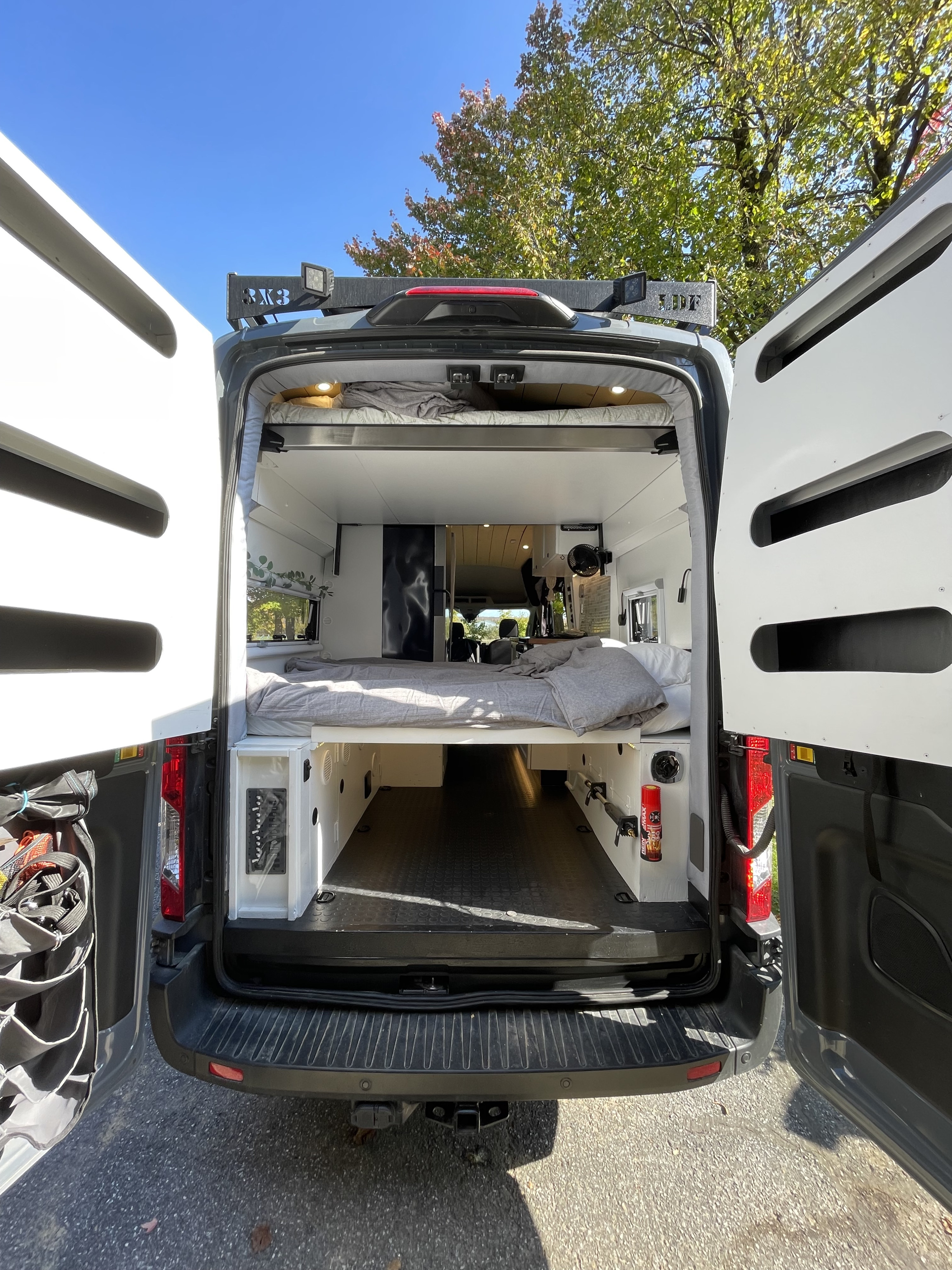 Spacious camper van interior, rear doors open, showing a cozy bed & ample storage. Ideal for an rv rental adventure.. Ford Transit 2023