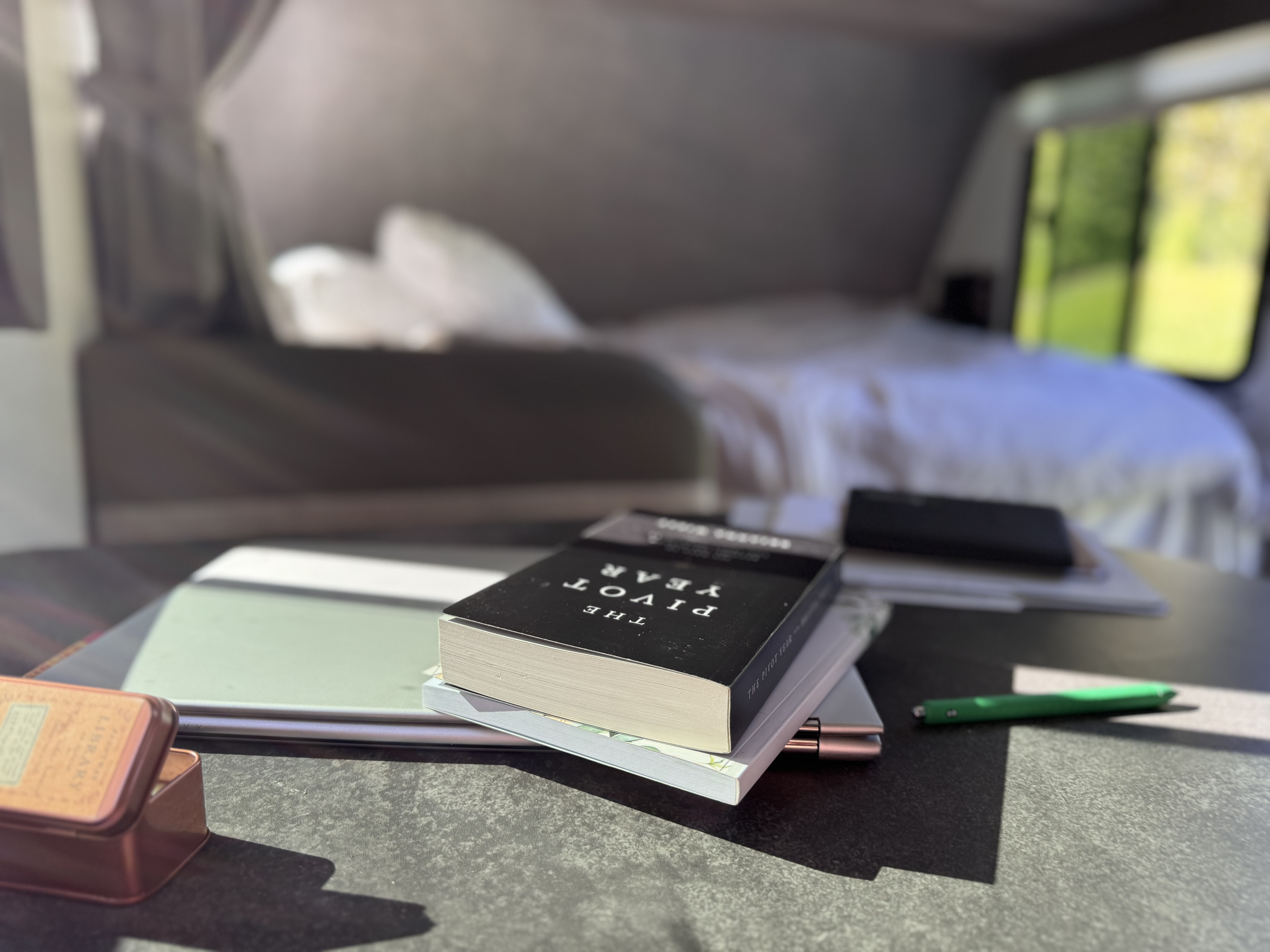 Inside an RV rental, a workspace setup with books, a laptop, and a pen on a table, with a cozy bed visible in the background.. Winnebago Minnie Winnie 2022