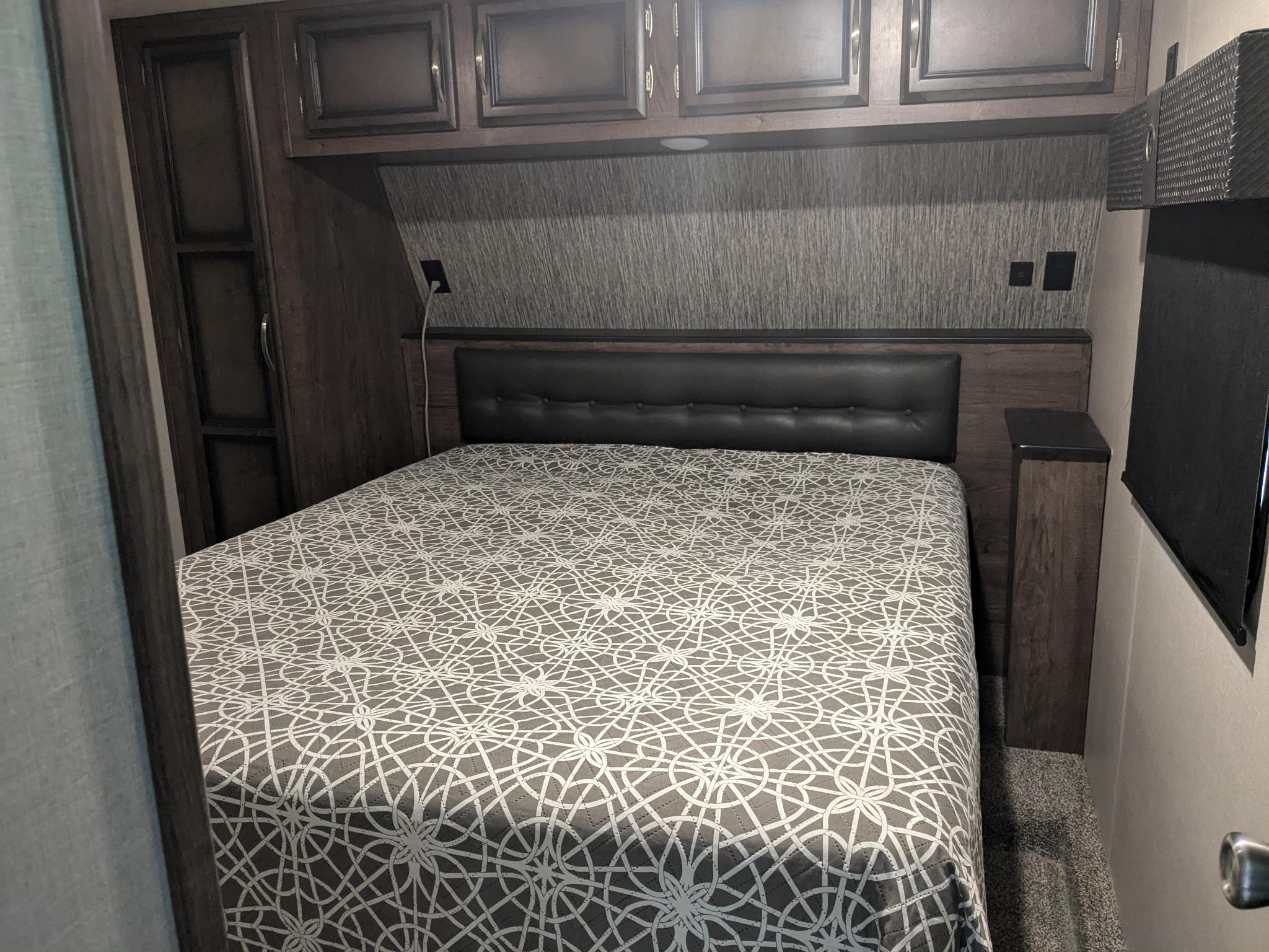 Cozy RV rental bedroom featuring a large bed with a geometric patterned comforter, overhead cabinets, and built-in storage.. K-Z Manufacturing Venom V3411TK 2020
