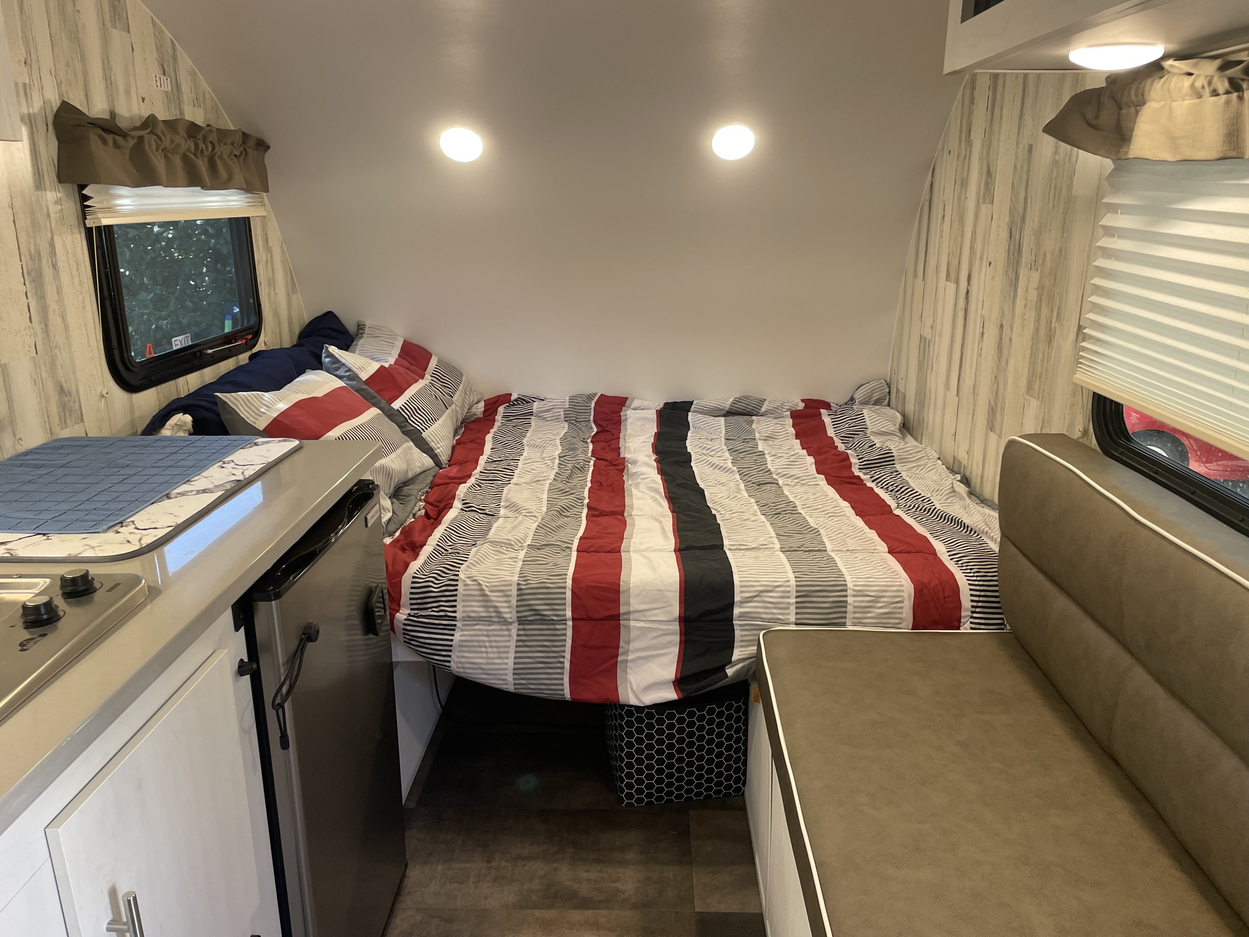 View inside an RV rental: striped bed, small kitchen, and dinette seat. A cozy, efficient living space for travel.. Travel Lite Rove Lite 2023