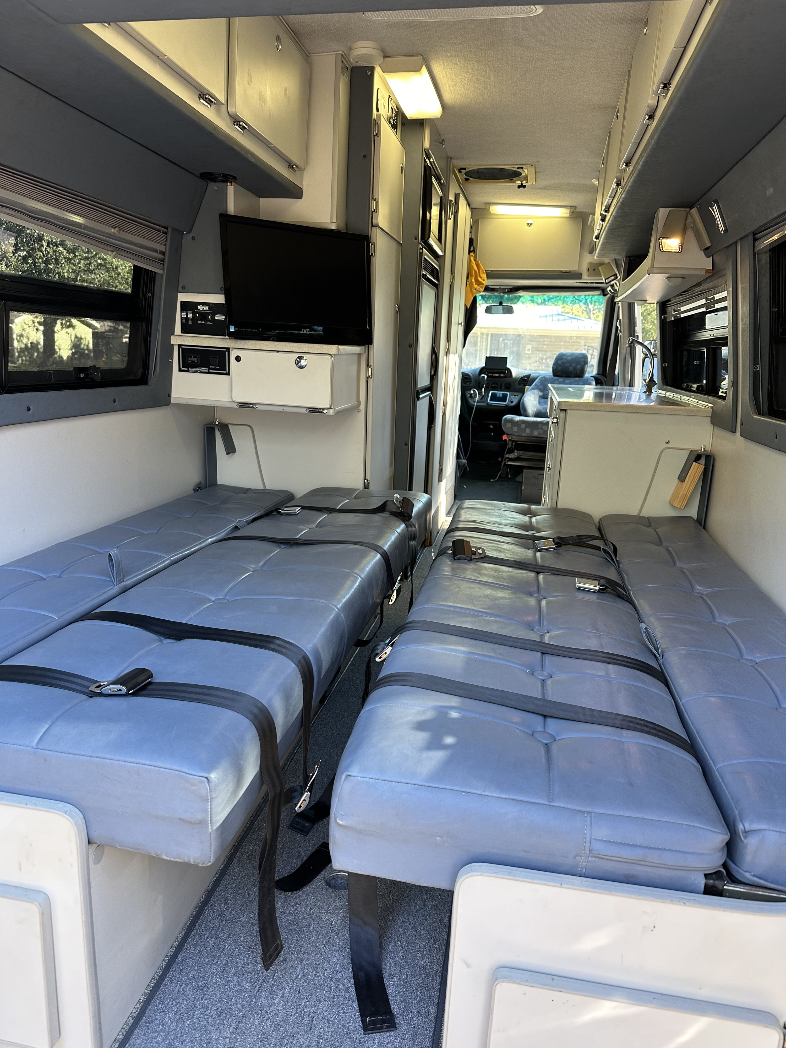 Inside an **rv rental** camper van: Two grey bench beds with belts, TV, and a sink area create a compact, functional living space.. Sportsmobile Custom Design 2006
