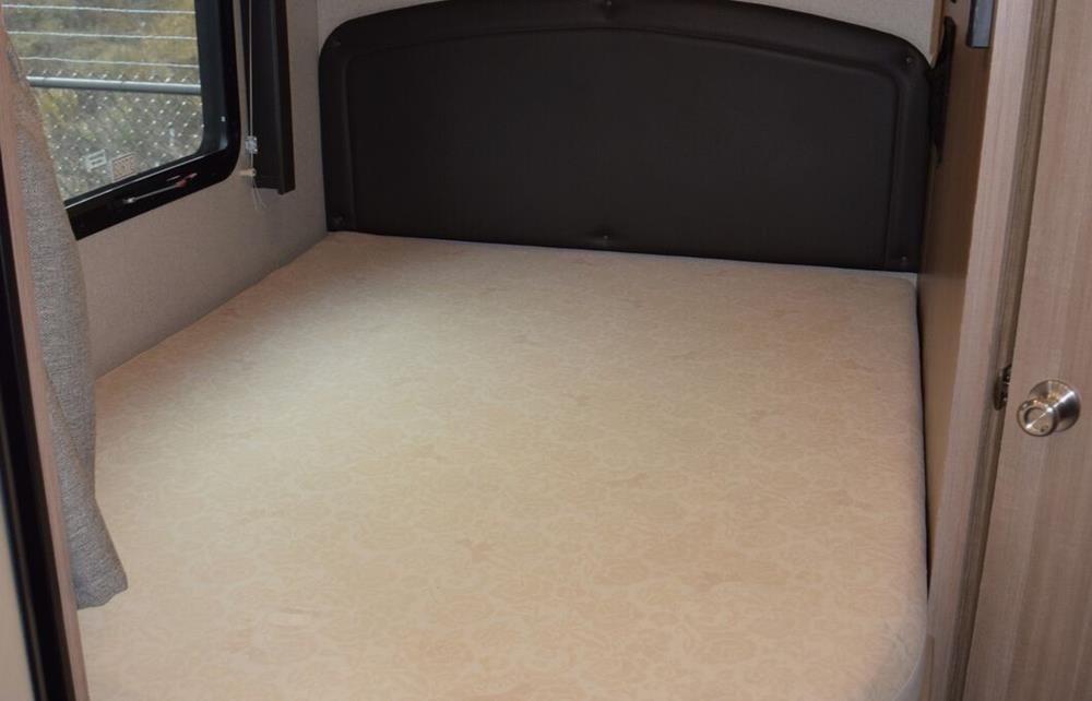 Compact RV rental bedroom featuring a light mattress, dark headboard, and window. Ideal for comfortable travel.. Adventurer Adventurer 2021