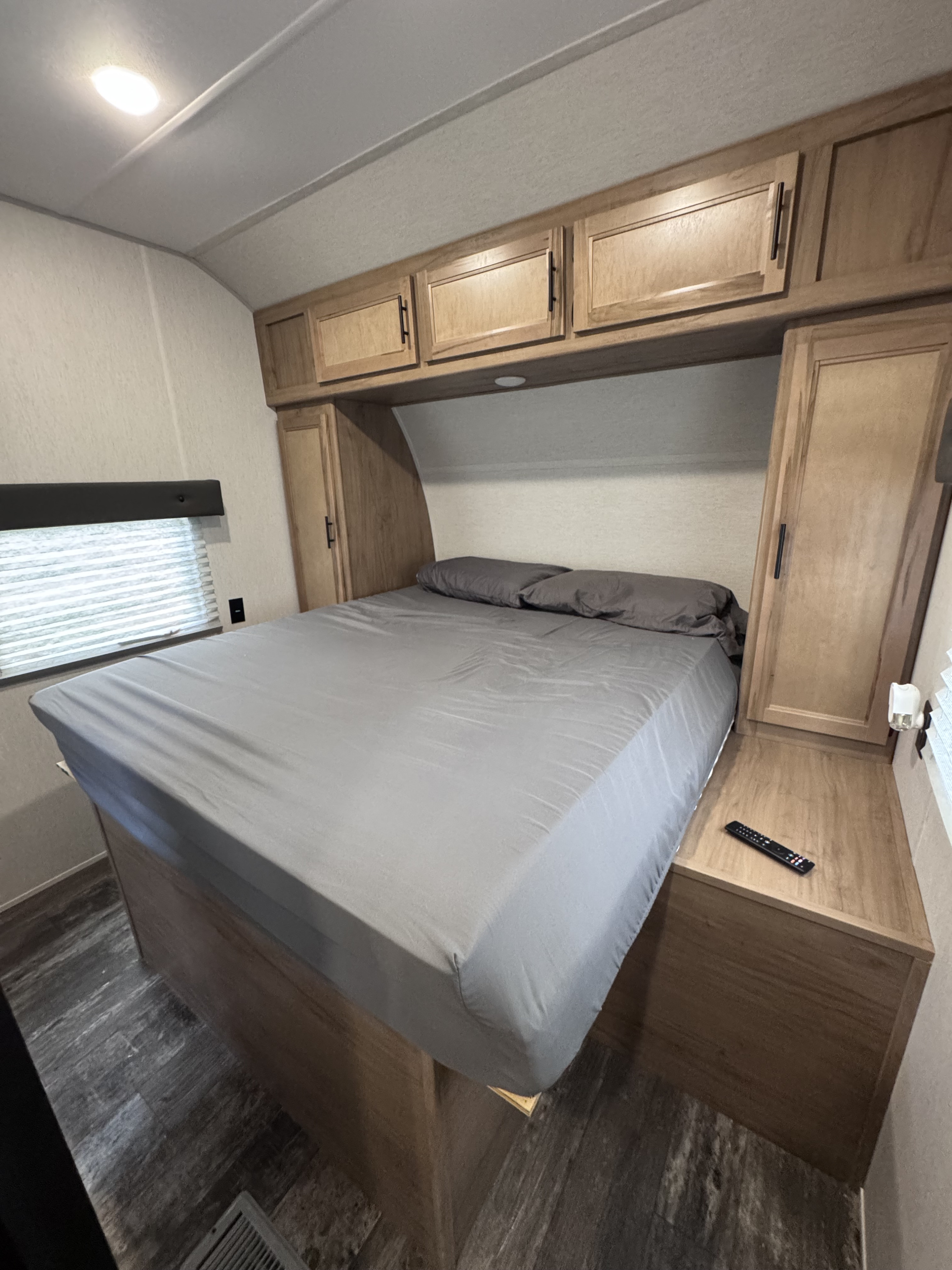 Compact RV rental bedroom with a bed, gray sheets, overhead and side wood storage, and lighting.. Forest River Vengeance 2024
