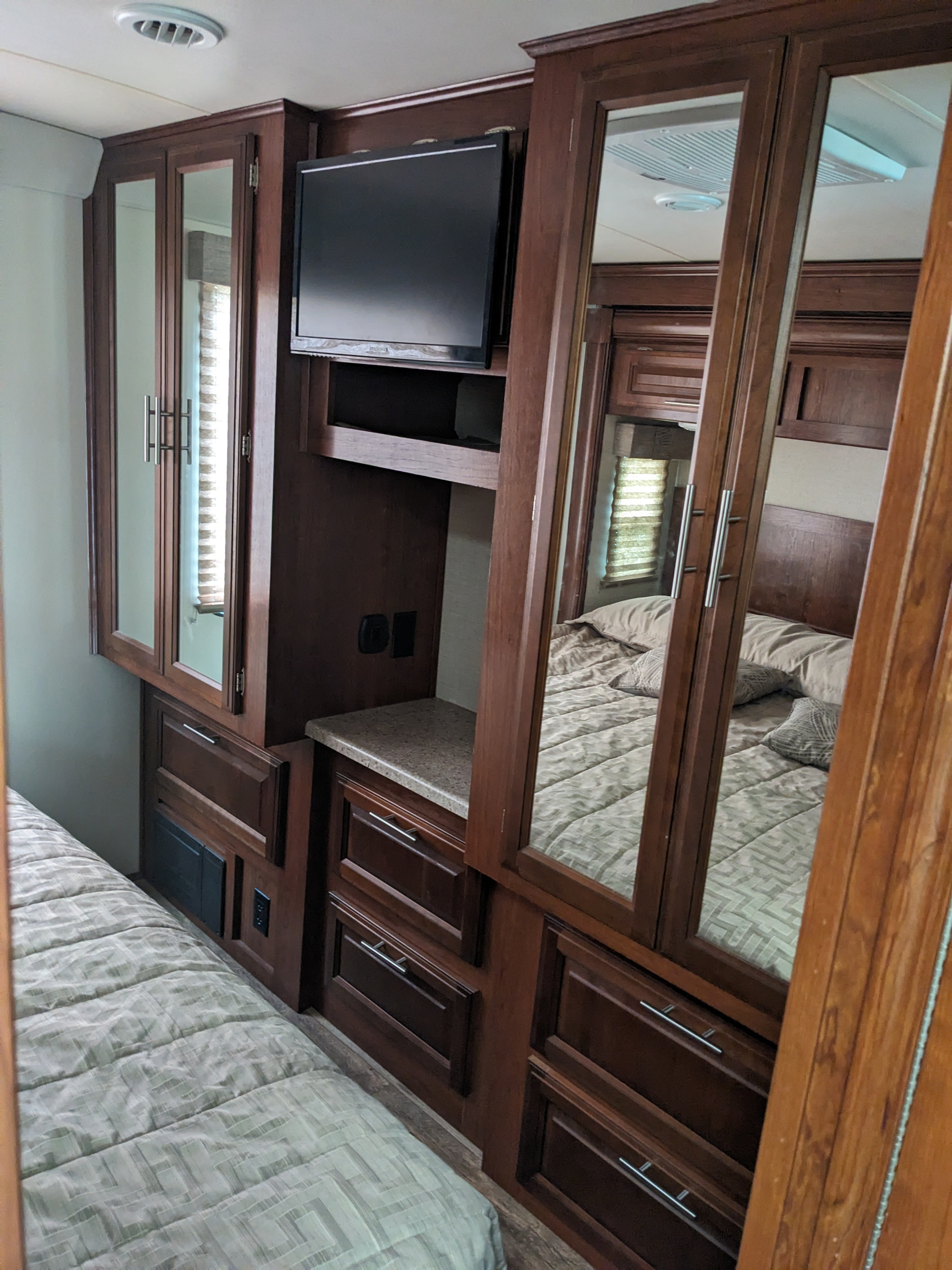 An RV rental bedroom showcasing dark wood cabinets, mounted TV, and a neatly made bed with a patterned comforter.. Forest River 30-DS 2018