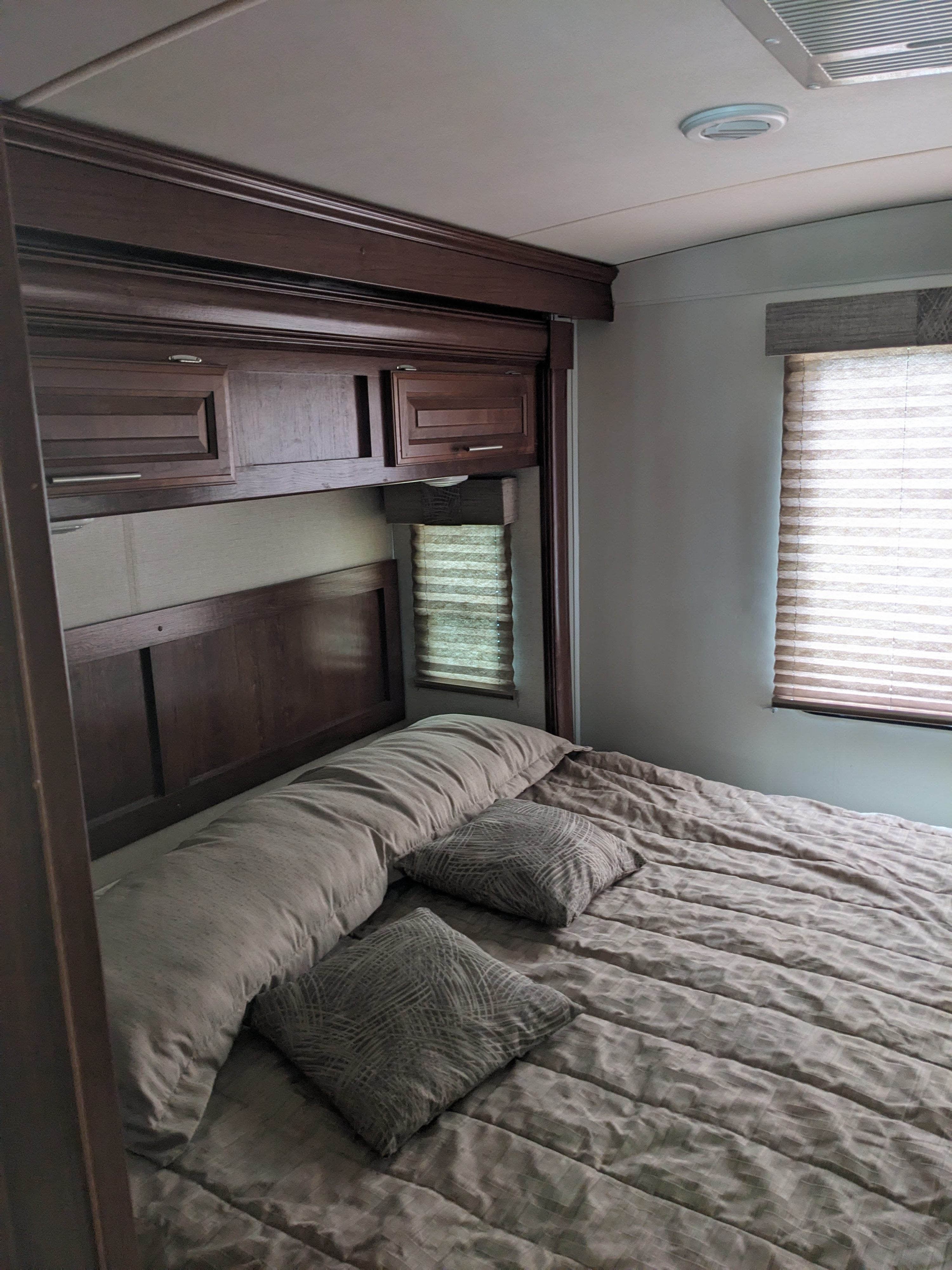 Cozy RV rental bedroom featuring dark wood cabinets, a comfortable bed with pillows, and window blinds for privacy.. Forest River 30-DS 2018