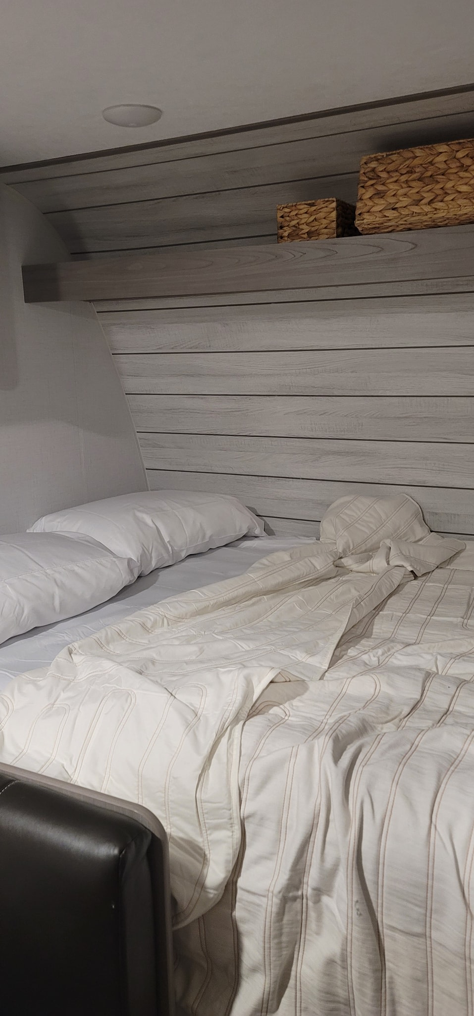 Inside an RV rental: a neat bed with white linens, wood paneling, and storage baskets on a shelf.. Dutchmen Coleman Lantern 17B 2024