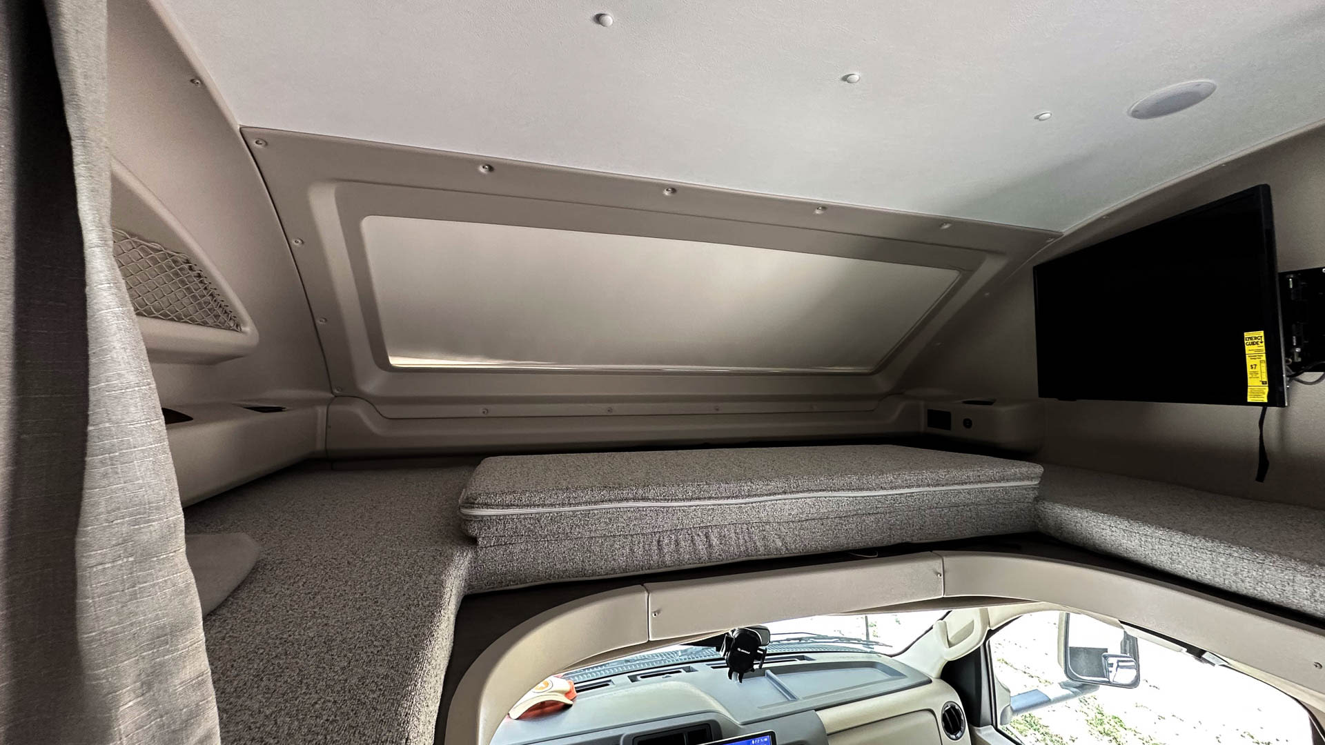RV rental interior: cab-over bunk with TV, cushions, and storage net, overlooking the driver's cab.. Entegra Coach Odyssey 2024