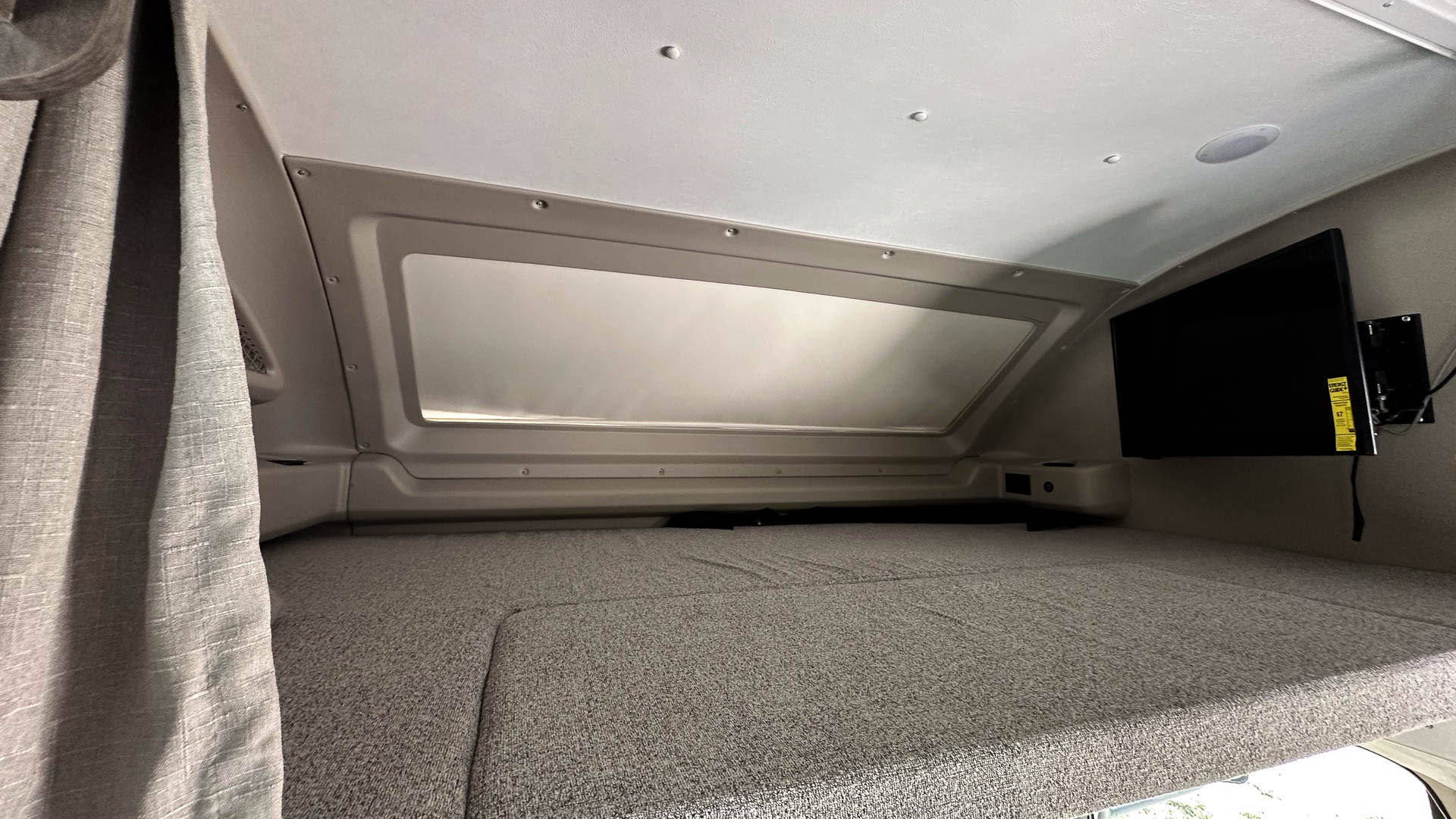Cozy RV rental overhead bunk bed with a mounted TV and window, offering a comfortable sleeping area inside.. Entegra Coach Odyssey 2024