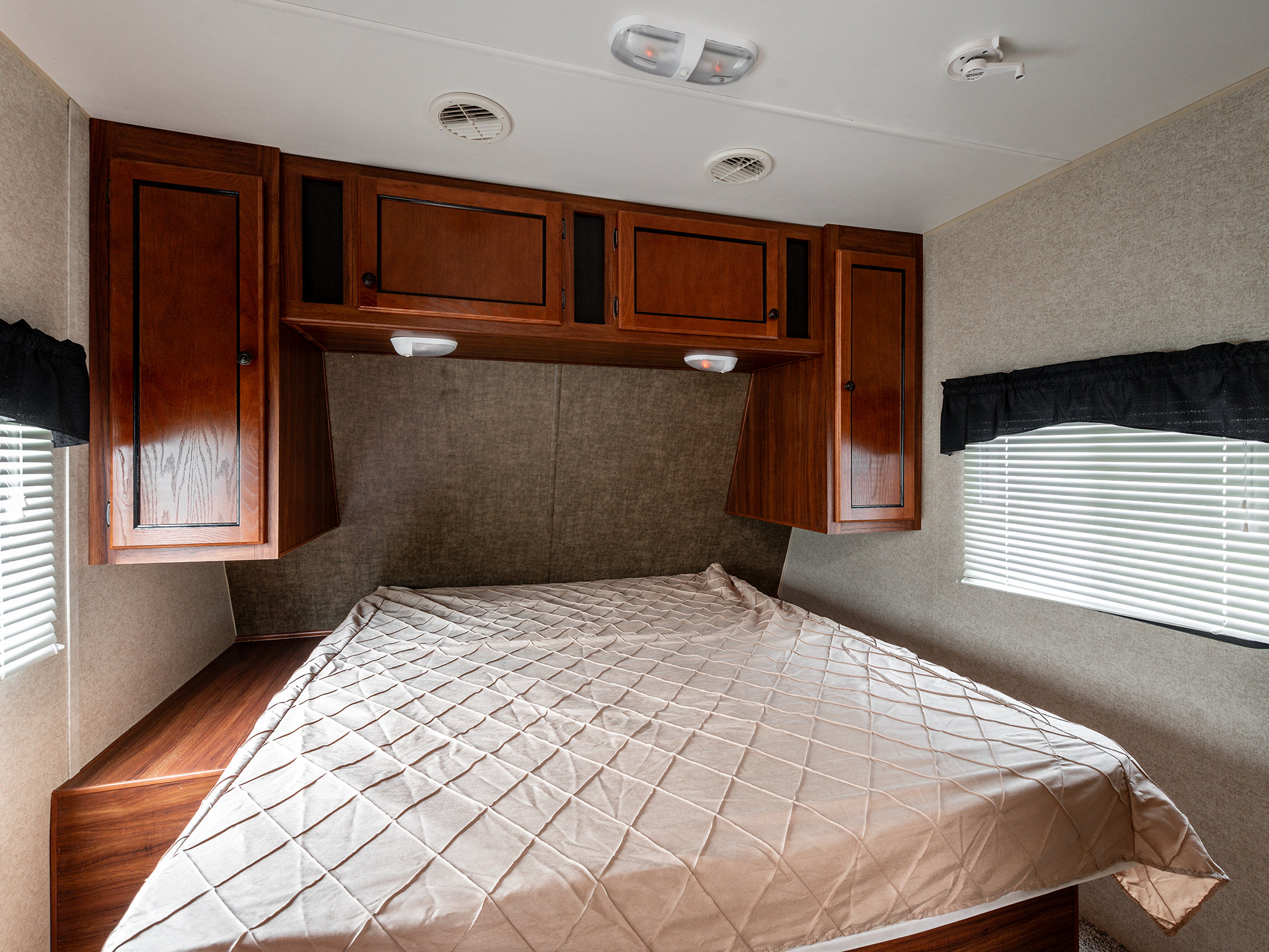 Comfortable RV rental bedroom with a large bed, rich wood cabinets, and bright windows for a cozy stay.. Heartland RVs Trail Runner 2015