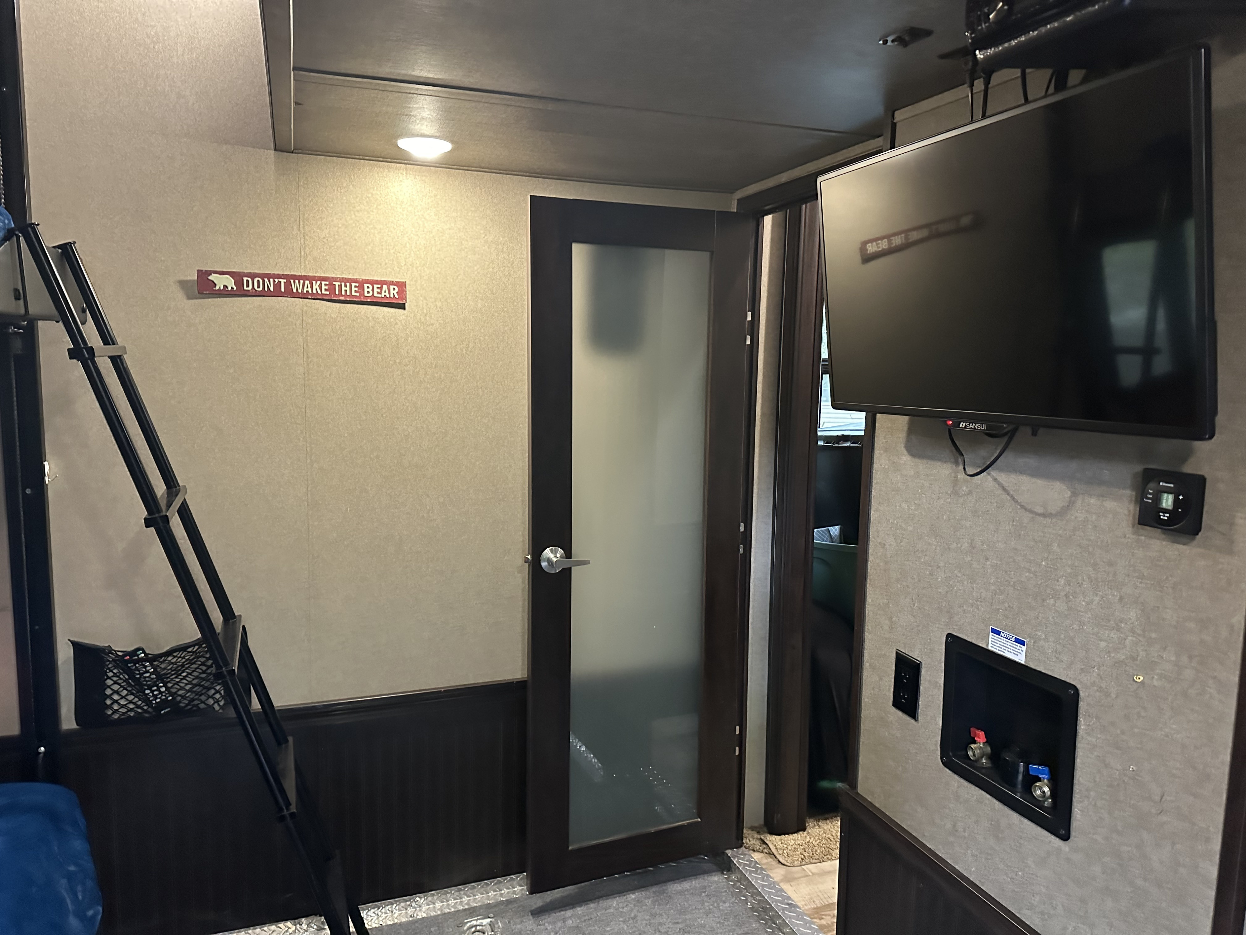 Inside an RV rental: ladder, "DON'T WAKE THE BEAR" sign, frosted door, TV, and washer hookups.. Forest River XLR Thunderbolt Toy Hauler 2017
