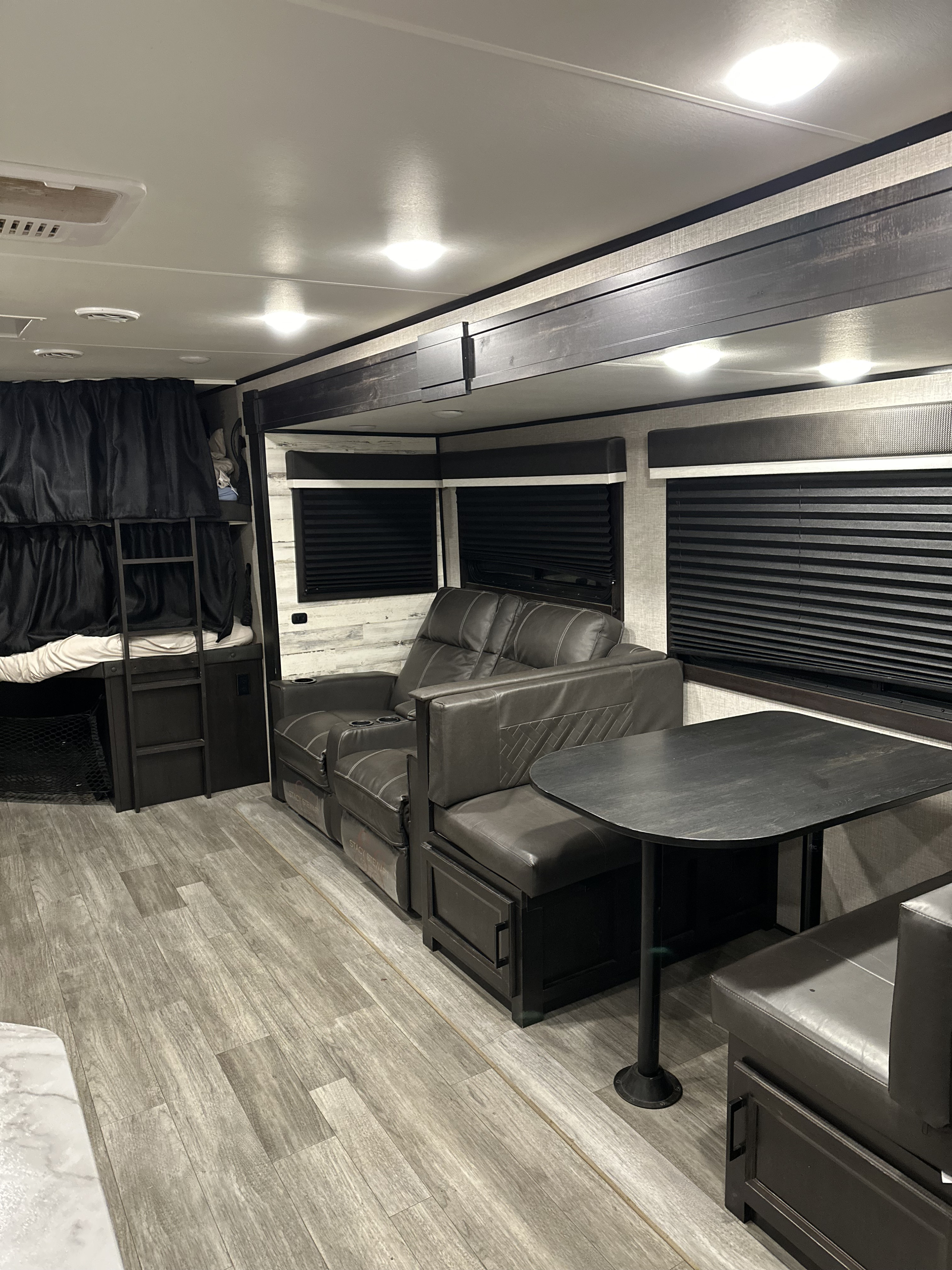 This RV rental interior features dark bunk beds, a comfy reclining sofa, and a dinette. A spacious and functional living area.. Jayco Jay Feather 2022