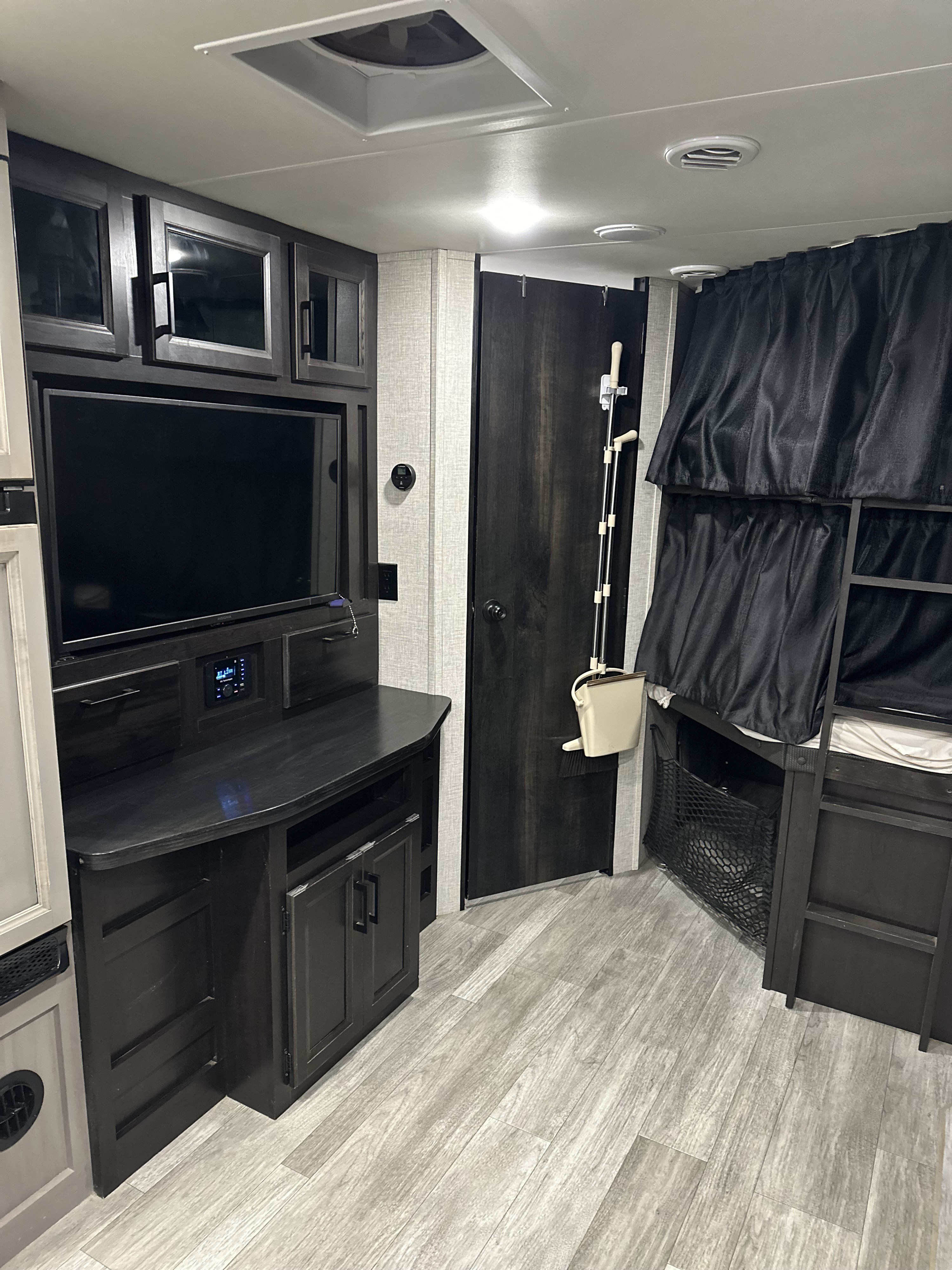 This RV rental interior features a sleek entertainment center, dark wood bunks with privacy curtains, and light flooring.. Jayco Jay Feather 2022