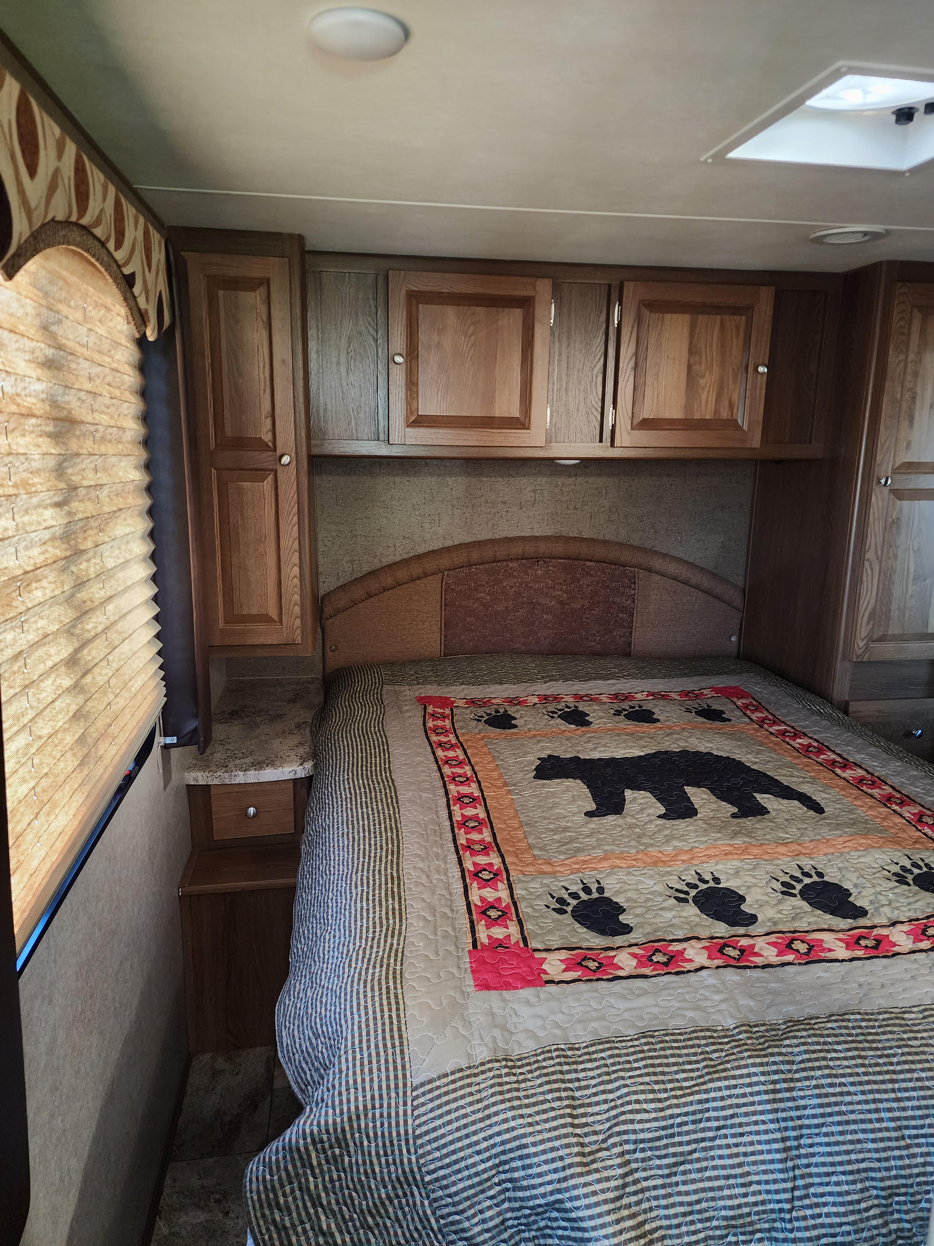 Cozy RV rental bedroom featuring a bed with a bear-themed quilt, wooden cabinets, and window blinds.. Forest River Coachmen Leprechaun 2016
