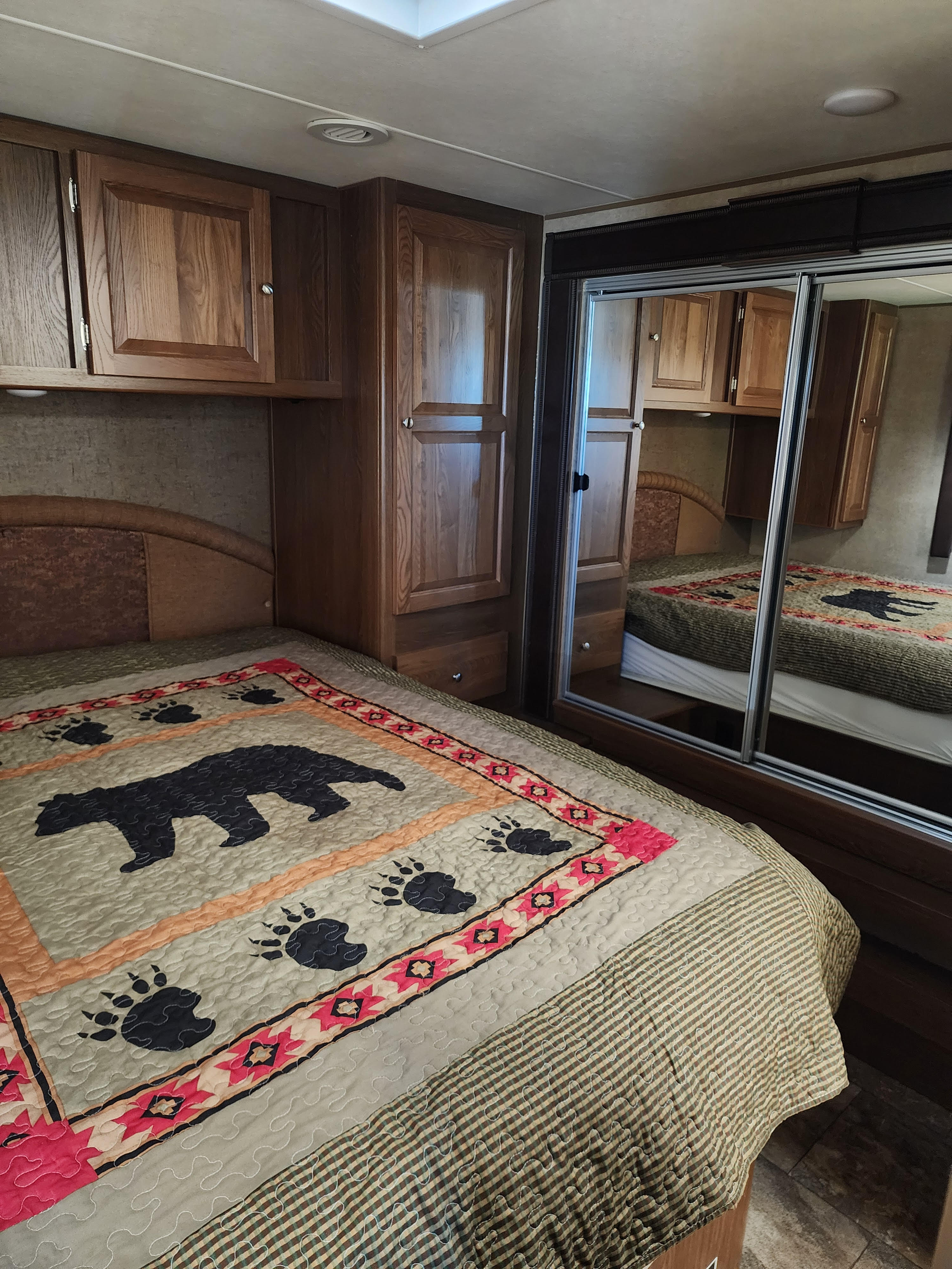 Cozy RV rental bedroom featuring a bear-themed quilt on the bed, wooden cabinets, and mirrored closet doors for compact living.. Forest River Coachmen Leprechaun 2016