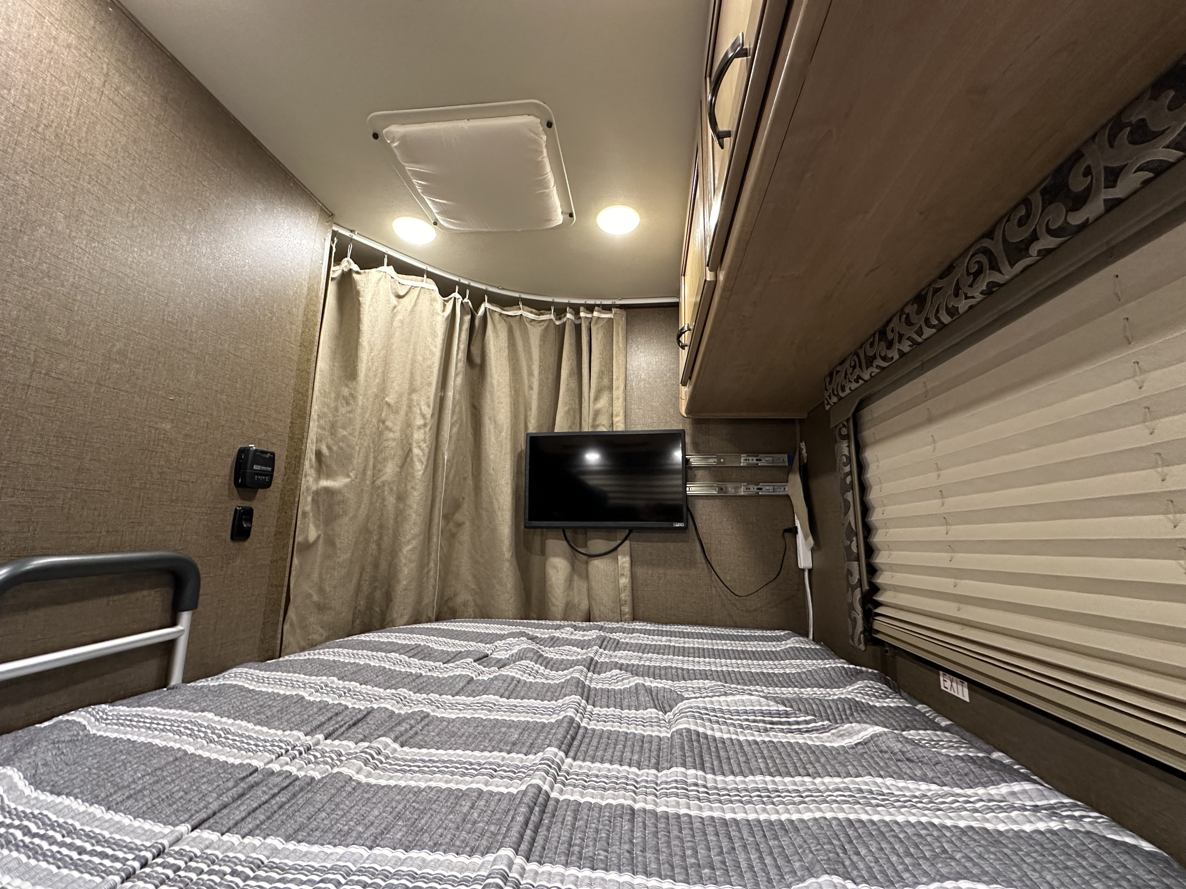Inside this **rv rental**: a compact bedroom with striped bed, TV, cabinets, and privacy curtains.. Thor Four Winds 2019
