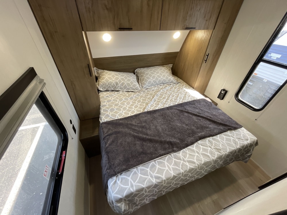 This RV rental's bedroom offers a cozy bed with patterned linens, overhead cabinets, and side windows.. Forest River Grey Wolf 29TE 2025