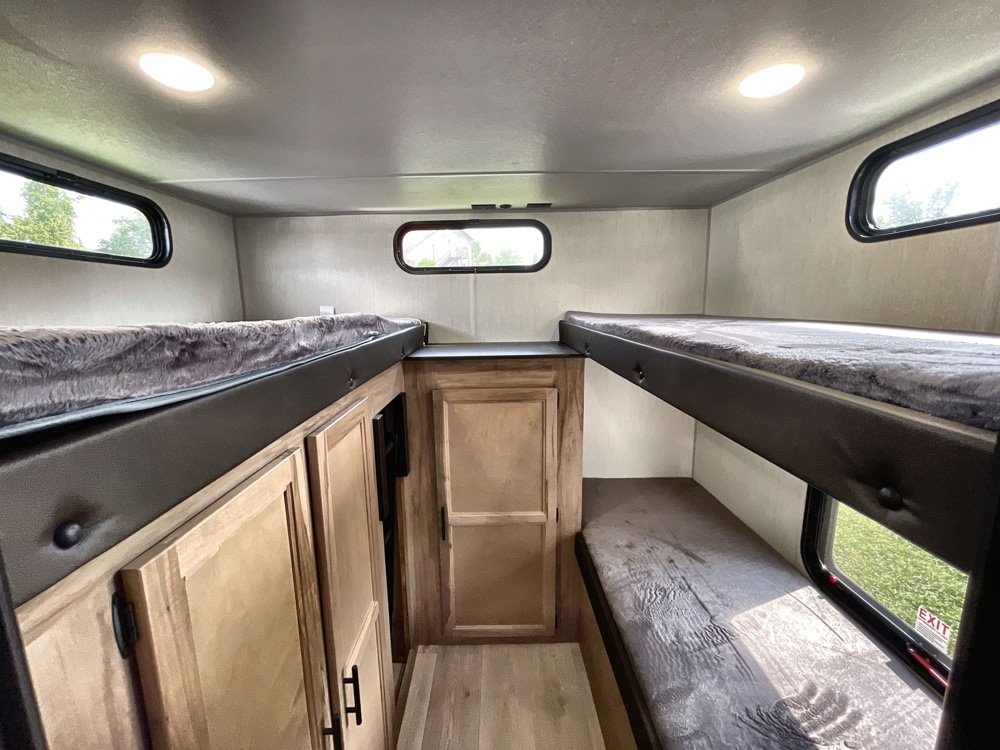 Inside an RV rental: two sets of bunk beds with plush mattresses, overhead lights, windows, and wood cabinetry.. Forest River Grey Wolf 29TE 2025