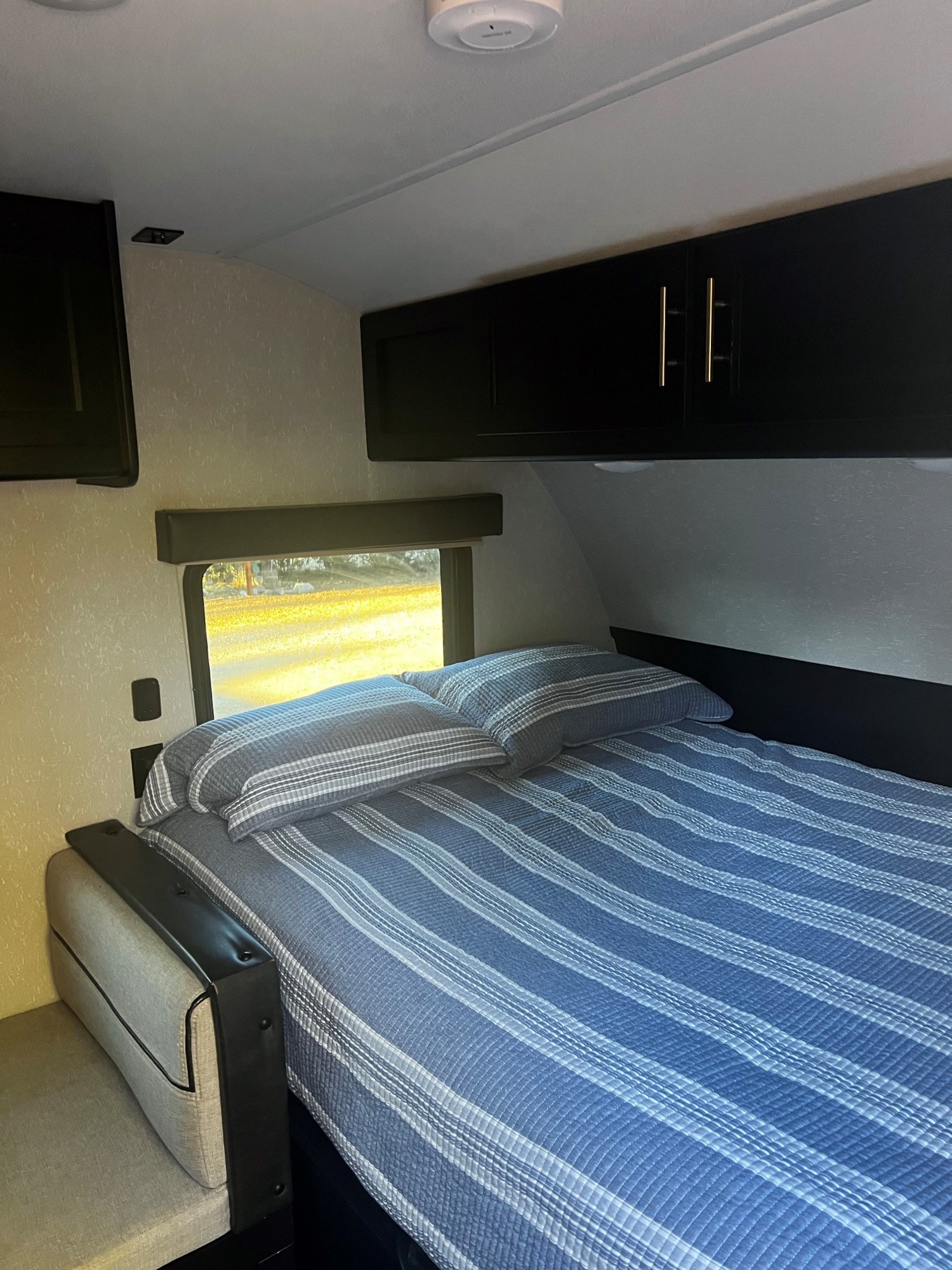 Inside an RV rental: compact bedroom with a striped bed, window view, and overhead cabinets for cozy travel.. Forest River Cherokee Wolf Pup Black Label 2021