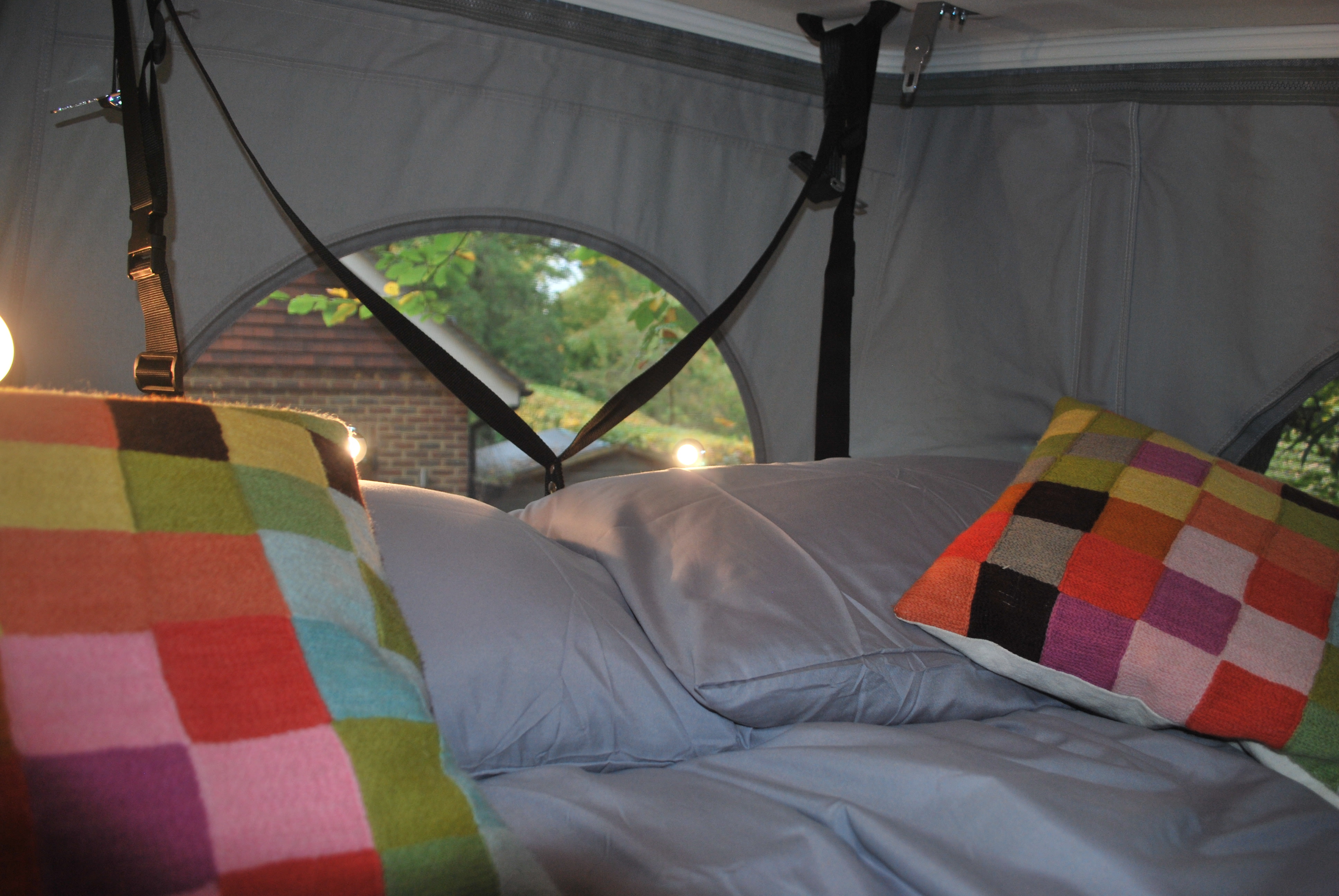 Cozy RV rental pop-top bed interior with colorful cushions and a view of nature through the arched window.. Auto Trail Expedition 67 2024