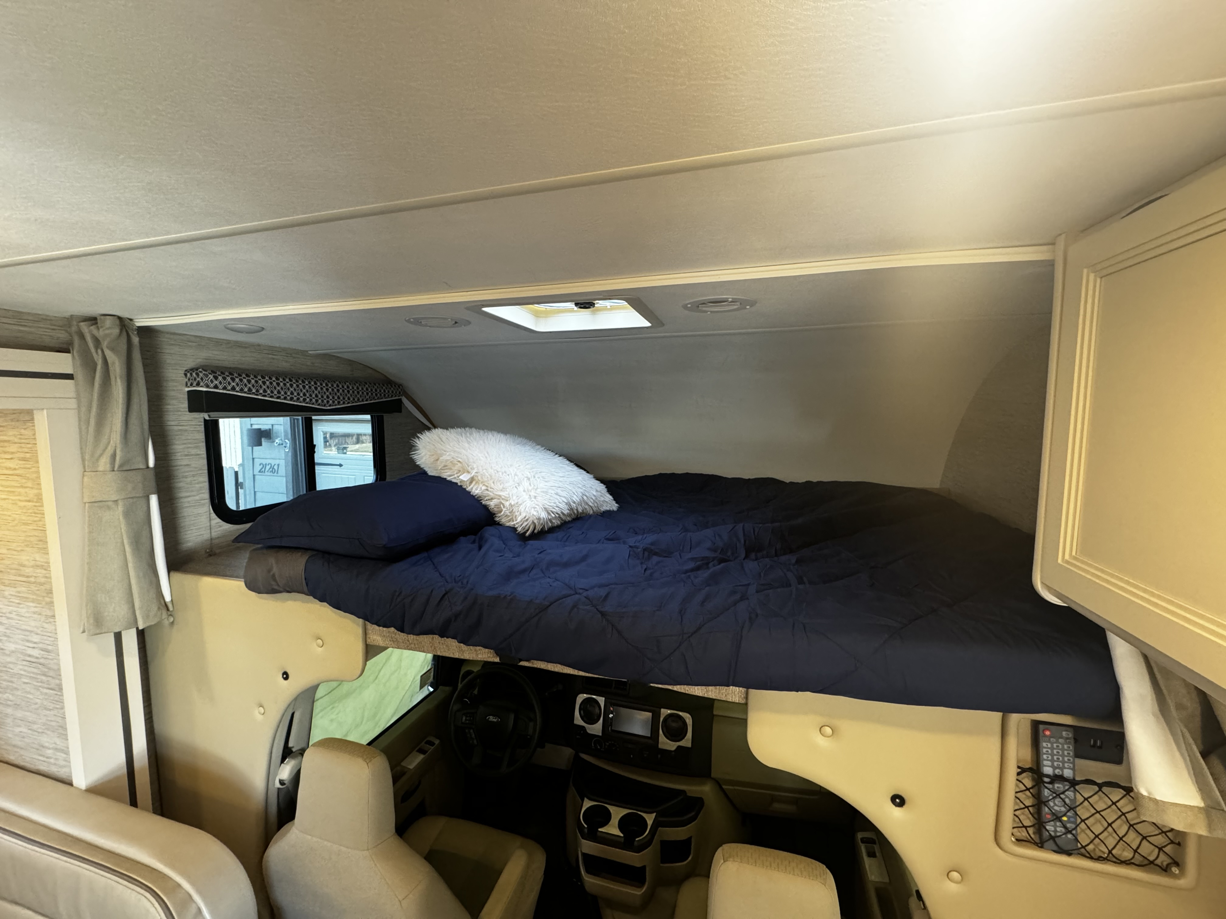 RV rental interior: A comfortable bed is visible above the driver's cab, featuring dark blue bedding and a window.. Thor Motor Coach Four Winds 2022
