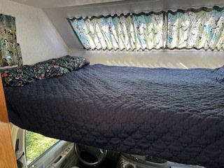 This RV rental offers a cozy overhead sleeping area with a dark blue quilted bed and patterned curtains, perfect for camping.. Shasta Cheyenne 2001