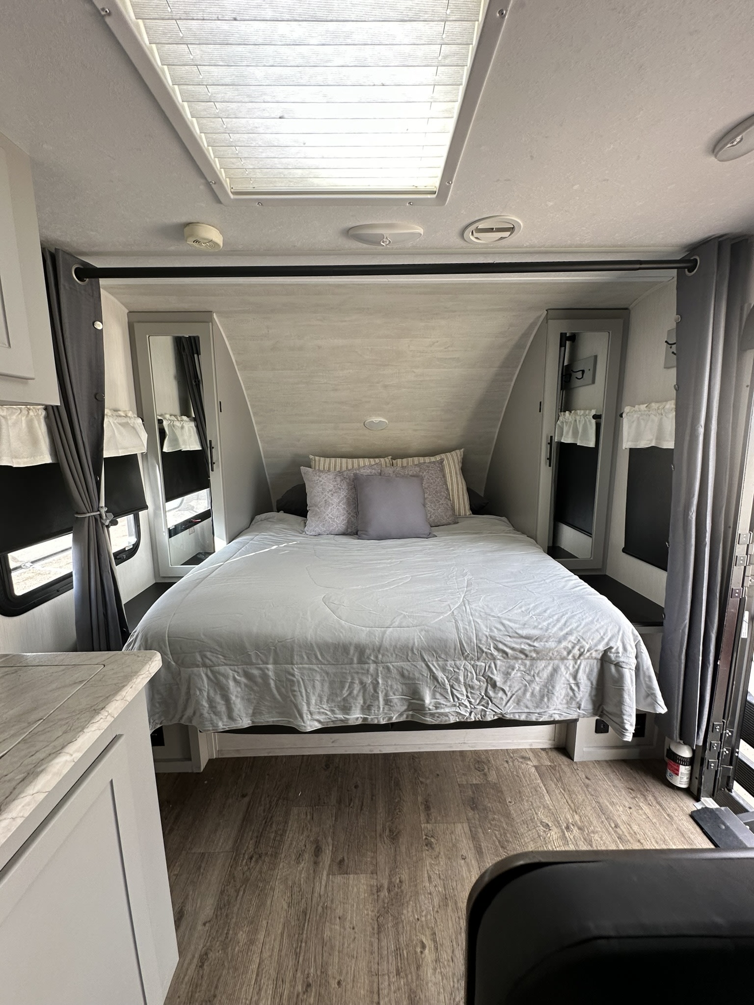 Experience comfort in this RV rental bedroom: large bed, overhead skylight, modern grey interior, and wood flooring.. Forest River Vibe 2021