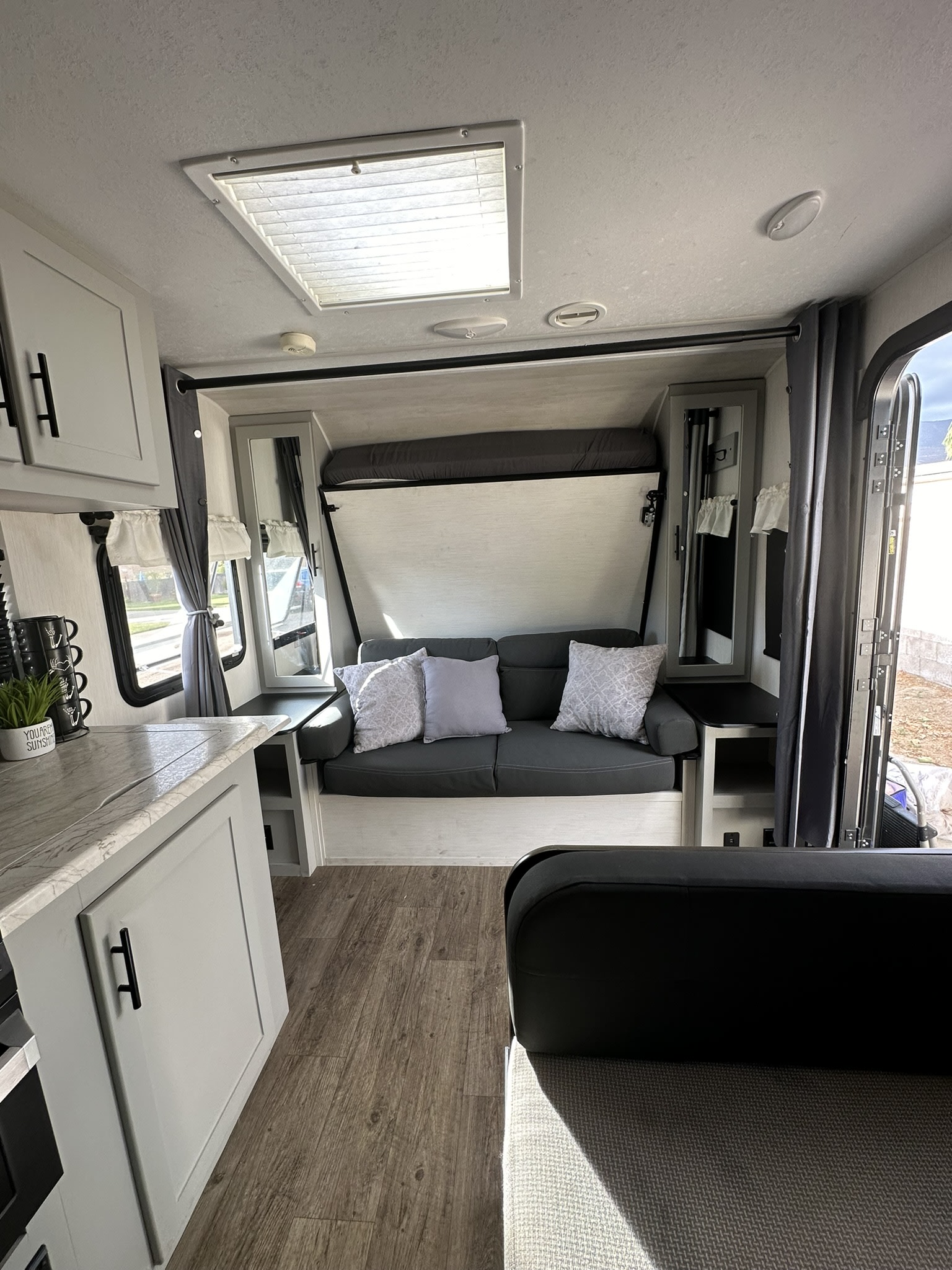 Inside a modern RV rental: living area with sofa, fold-down bed, kitchen counter, & skylight.. Forest River Vibe 2021