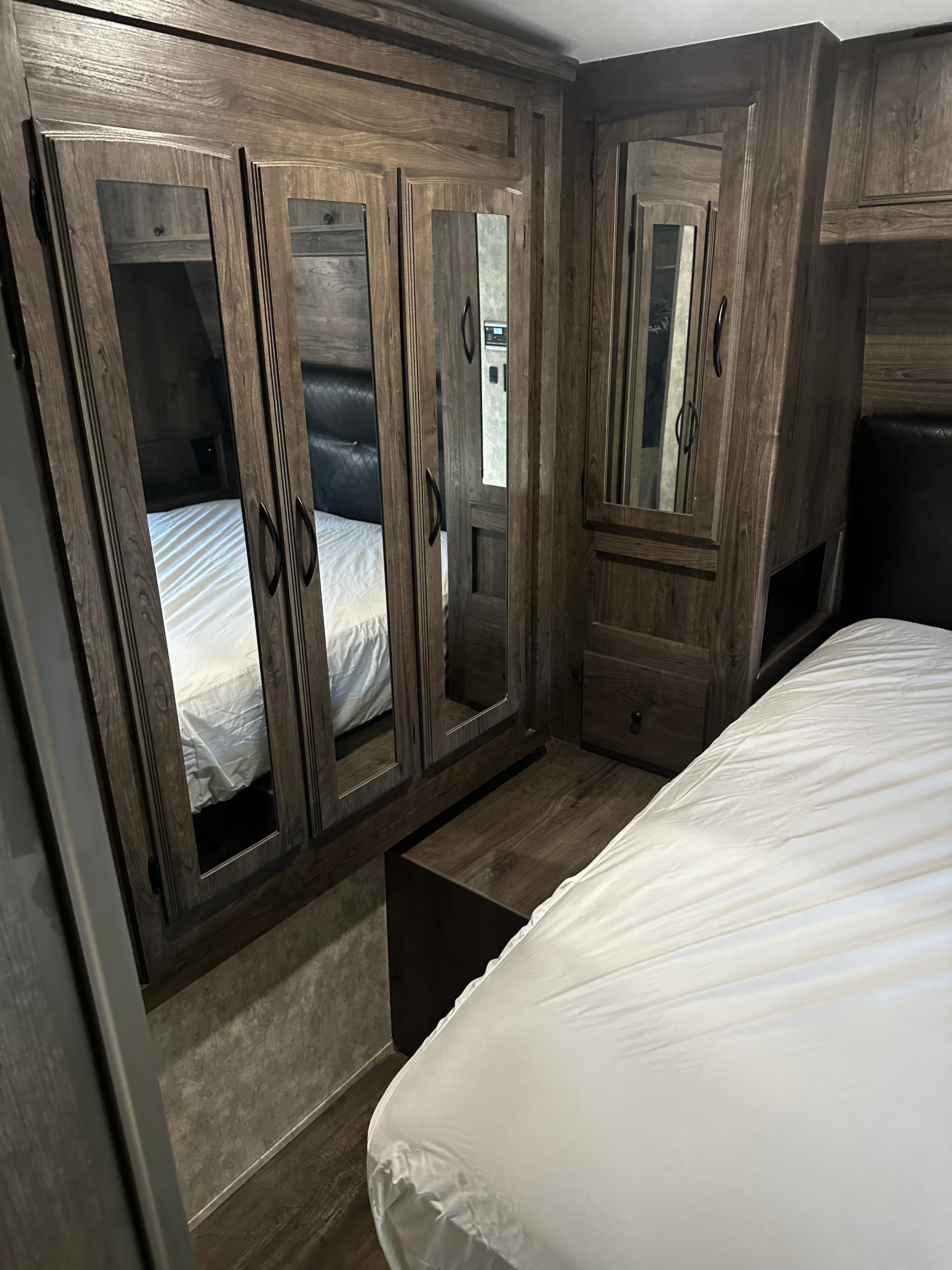 Dark wood cabinetry and mirrored closet doors flank a bed with white sheets in this RV rental bedroom.. Eclipse Recreational Vehicles Attitude 2018