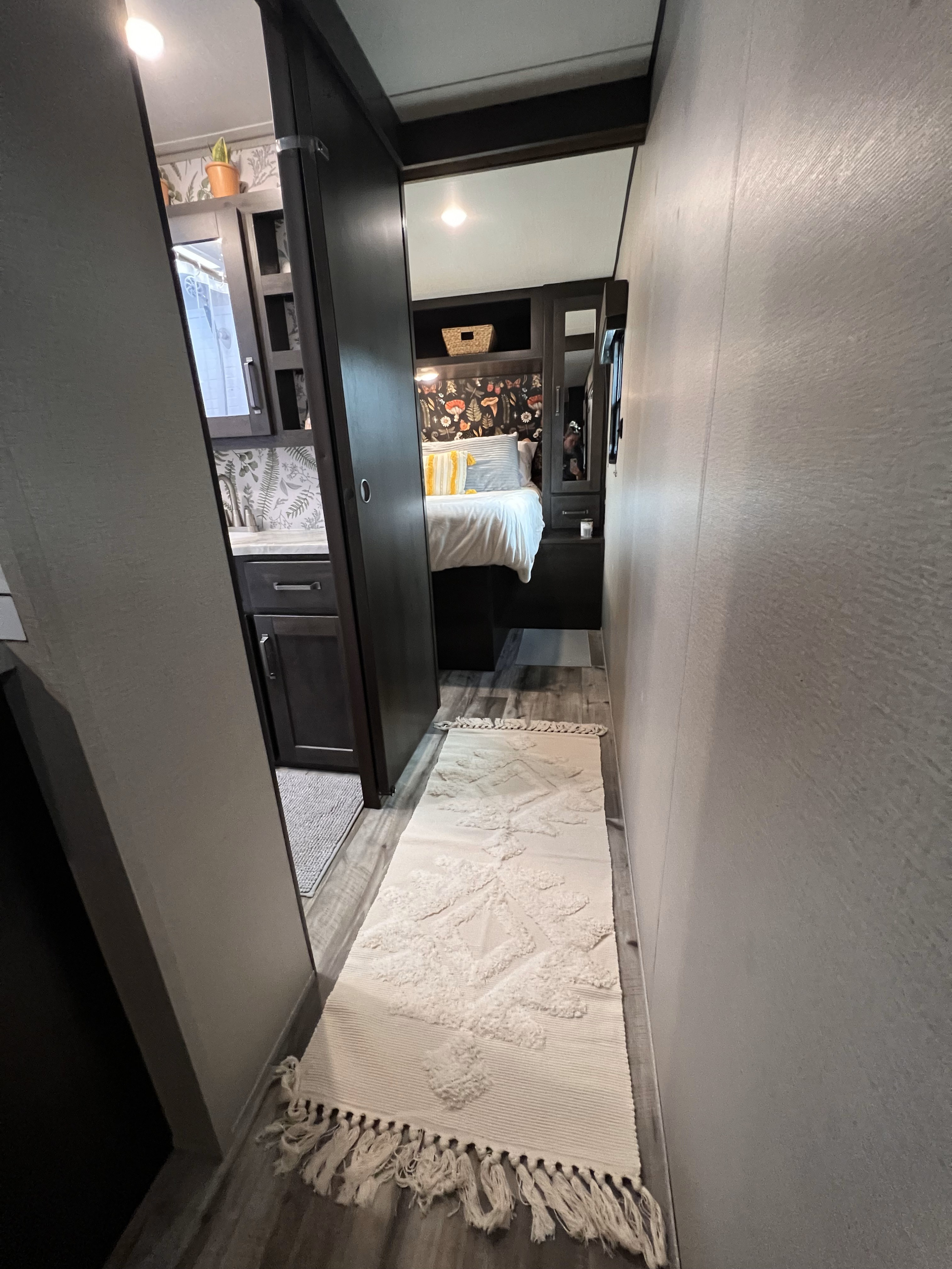 Discover this cozy RV rental interior. Hallway with a textured rug leads to an inviting bedroom and a peek into the bathroom.. Grand Design Transcend Xplor 2022