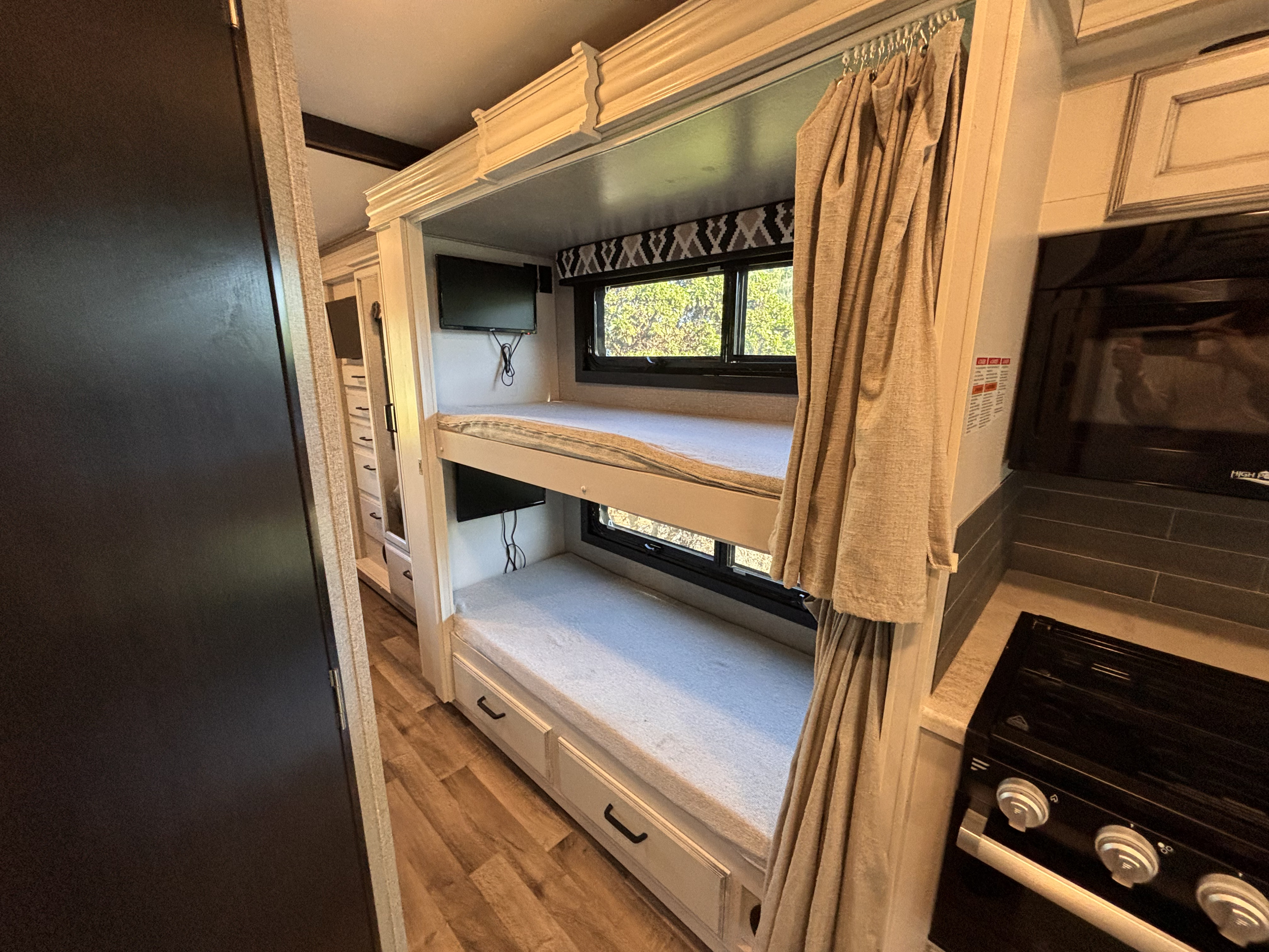 Spacious RV rental features comfy bunk beds with individual TVs, and a compact kitchen area to the right.. Jayco Alante 2021