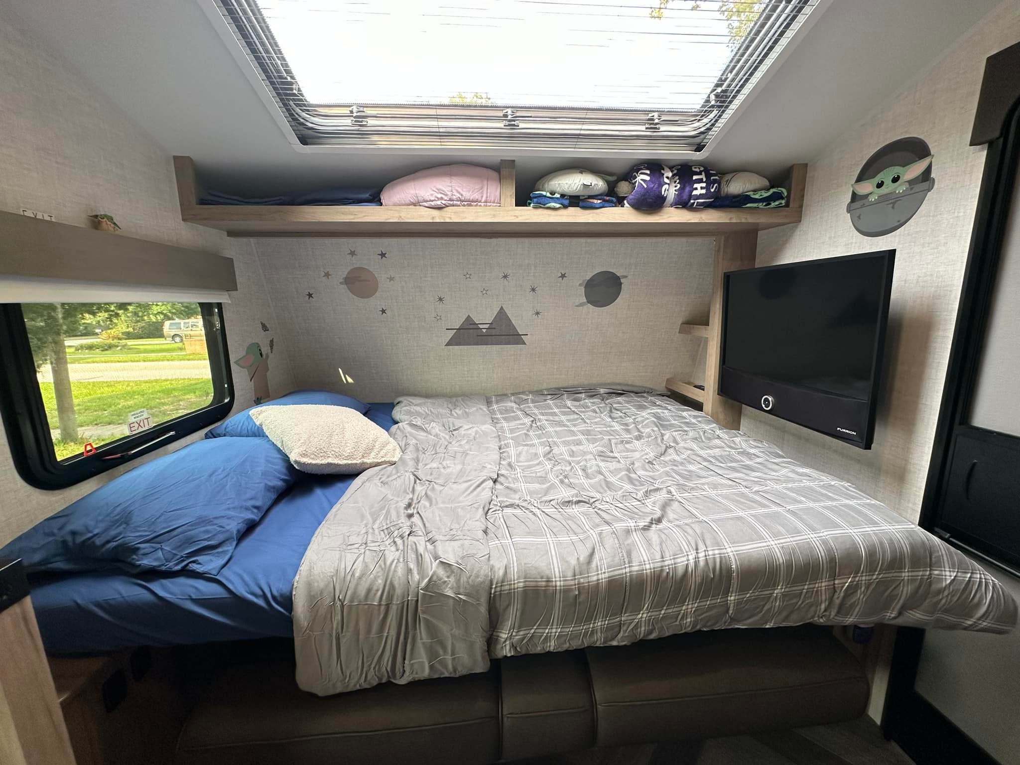 Cozy RV rental bedroom with a large bed, overhead skylight, mounted TV, and fun Grogu decor. Includes window views.. Ember 191MBD 2022