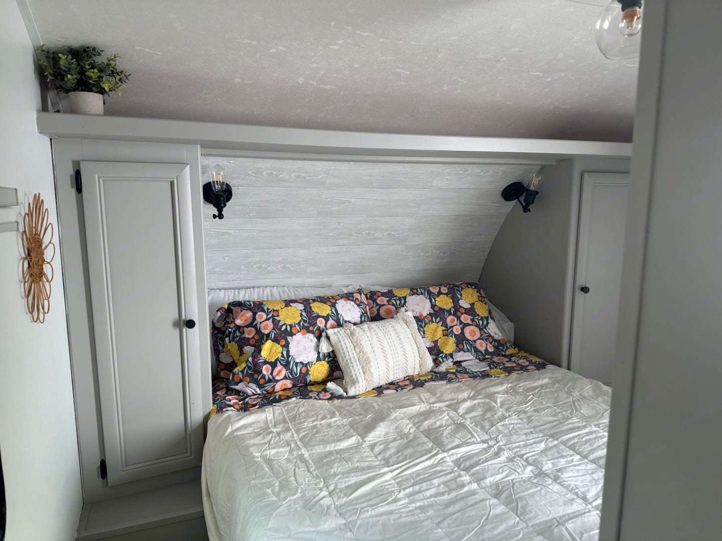 Cozy RV rental bedroom featuring floral bedding, wall sconces, and built-in storage. Ideal for comfortable travel.. Shasta 305QB 2015