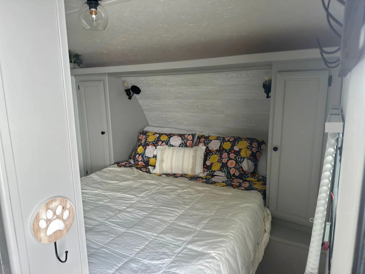 Comfortable RV rental bedroom featuring a bed with floral bedding, built-in cabinets, and a charming paw print hook.. Shasta 305QB 2015