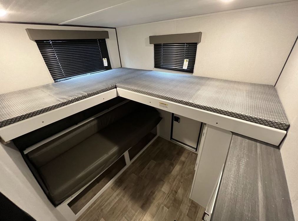 Compact RV rental interior with L-shaped bunk beds, a lower dinette, and a small fridge for efficient space utilization.. Keystone Hideout 2022