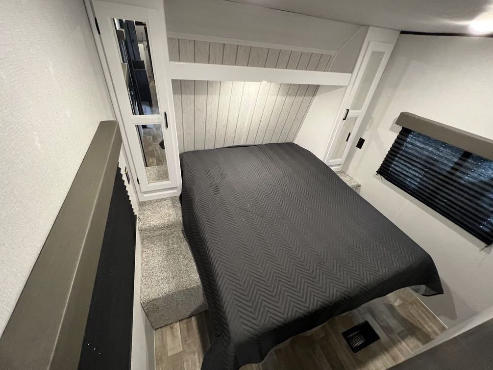 Cozy RV rental bedroom with a comfortable bed, built-in storage, wood-paneled wall, and window blinds.. Keystone Hideout 2022