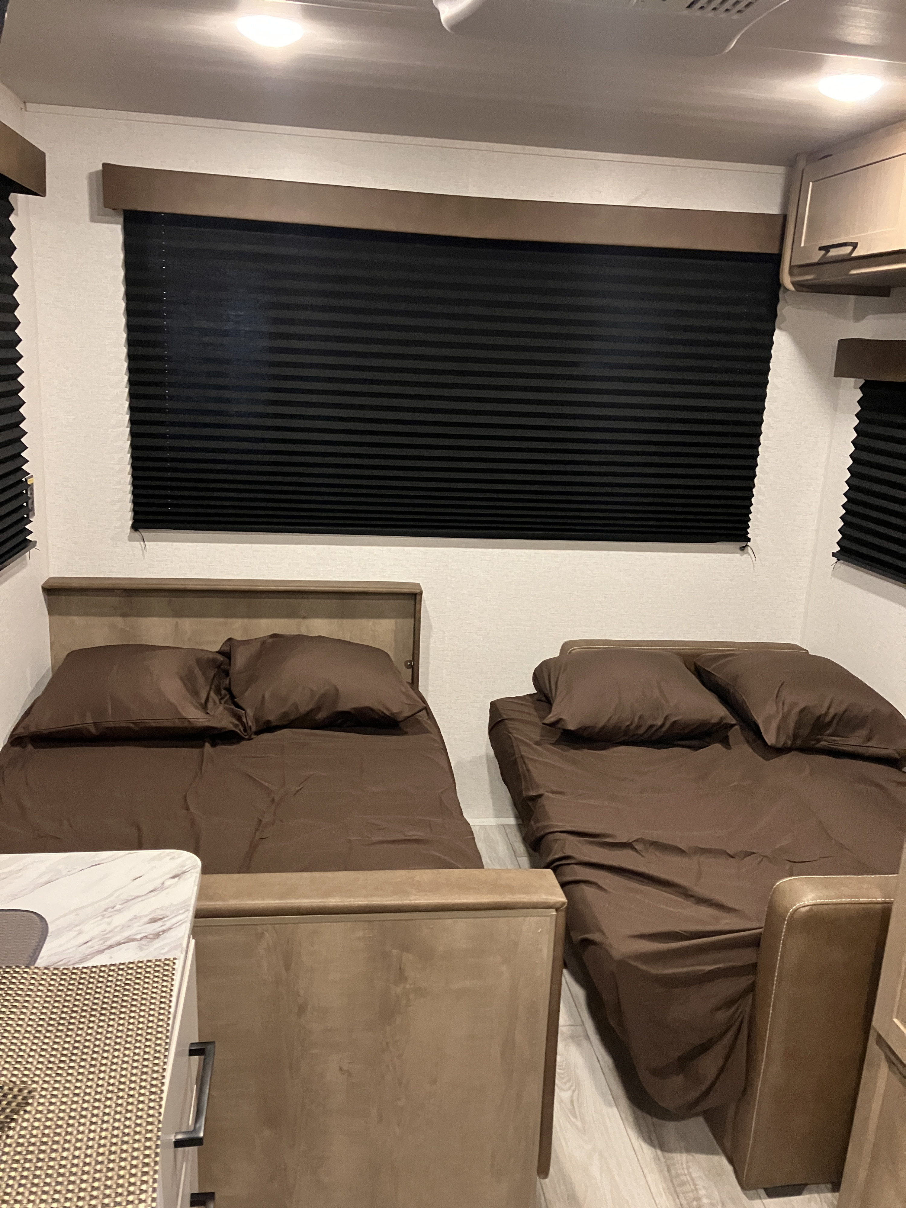 This RV rental features a cozy sleeping area with two comfortable beds, brown linens, and black privacy blinds.. Keystone Springdale 200RLC 2025