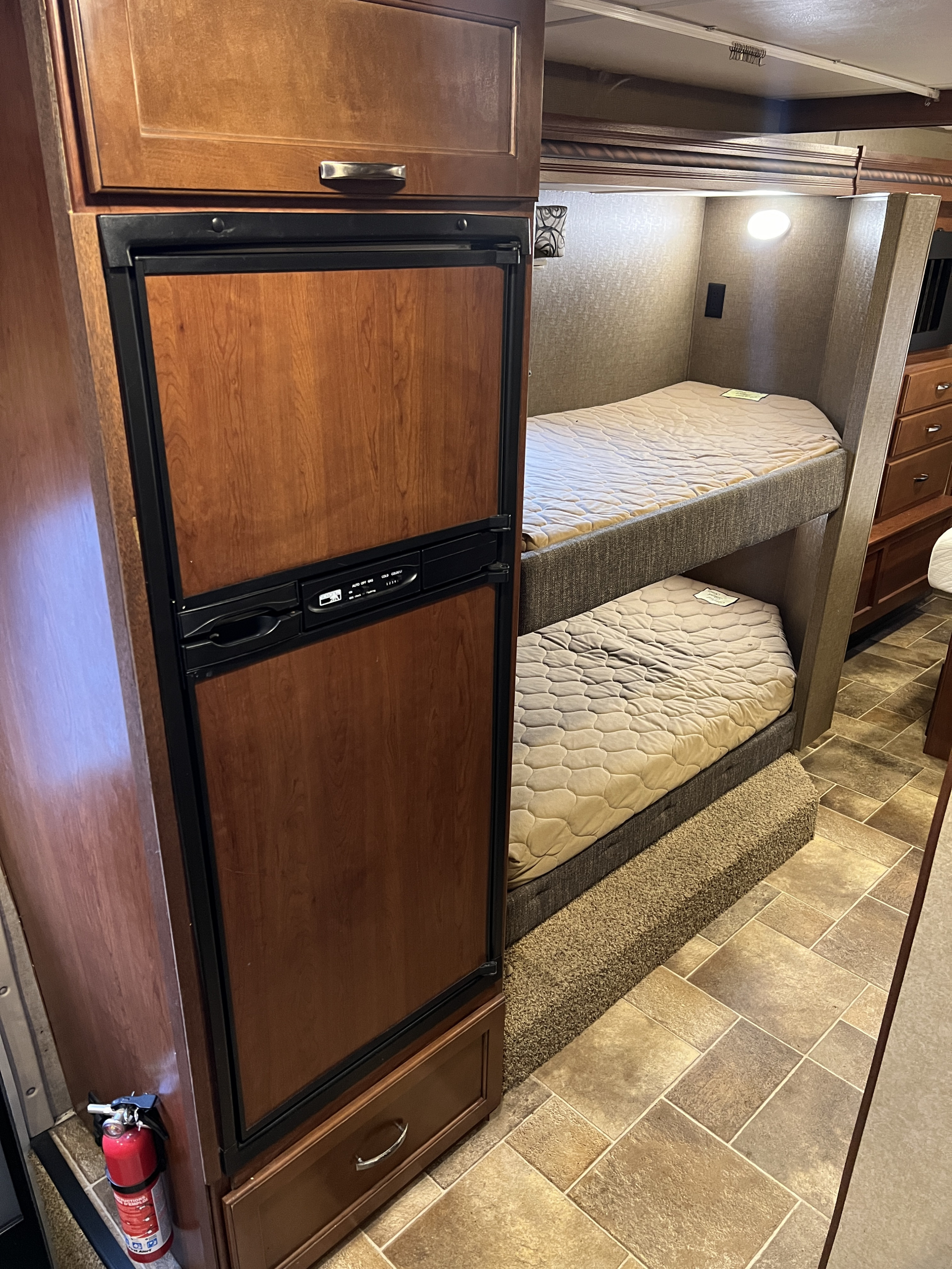 Experience an RV rental! This cozy interior shows a wooden refrigerator, bunk beds, and a fire extinguisher for safety.. Thor Motor Coach Four Winds 2017
