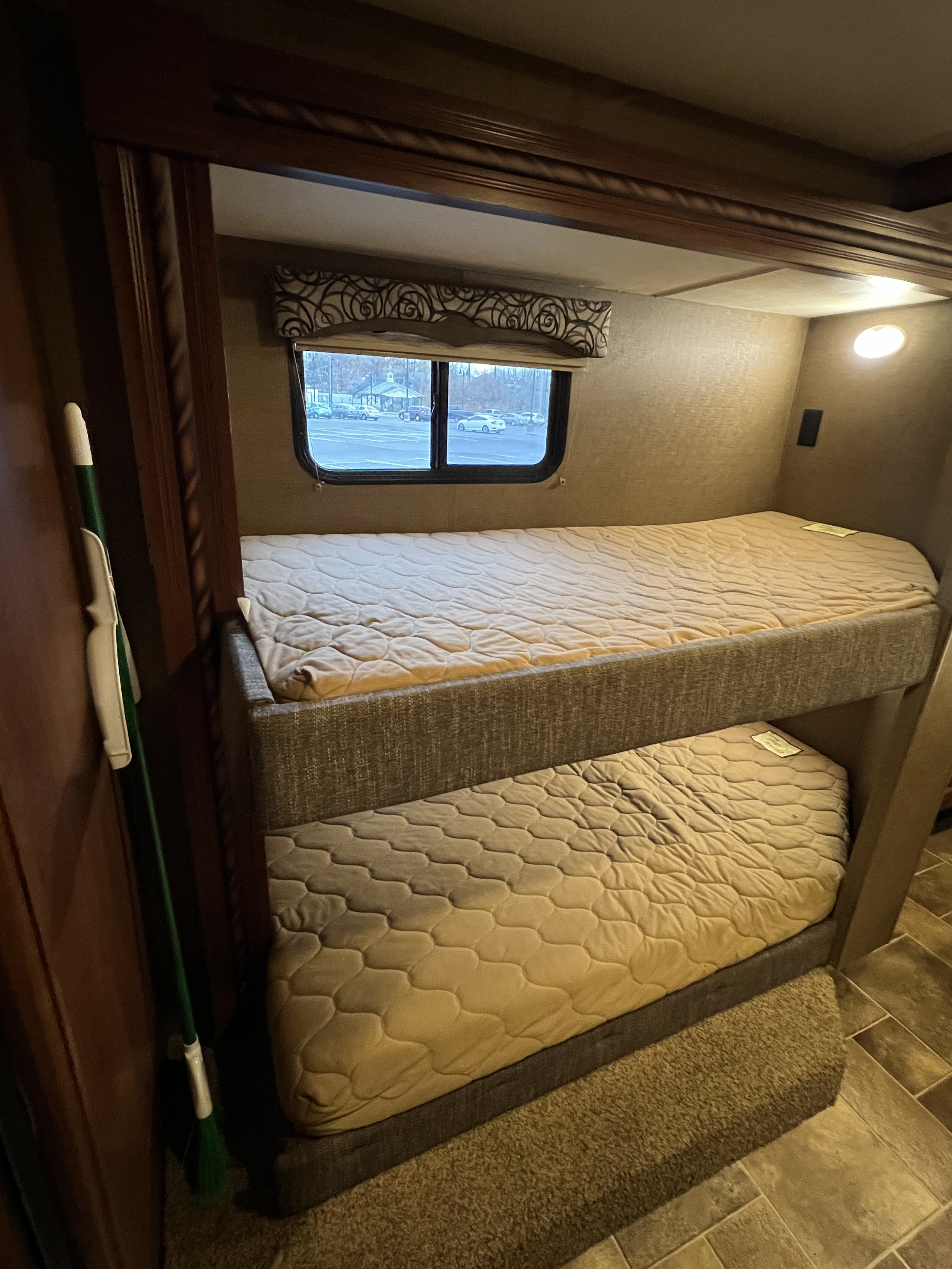 RV rental interior: cozy bunk beds with quilted mattresses, a window view of a parking lot, and carpeted floor. Ready for travel.. Thor Motor Coach Four Winds 2017